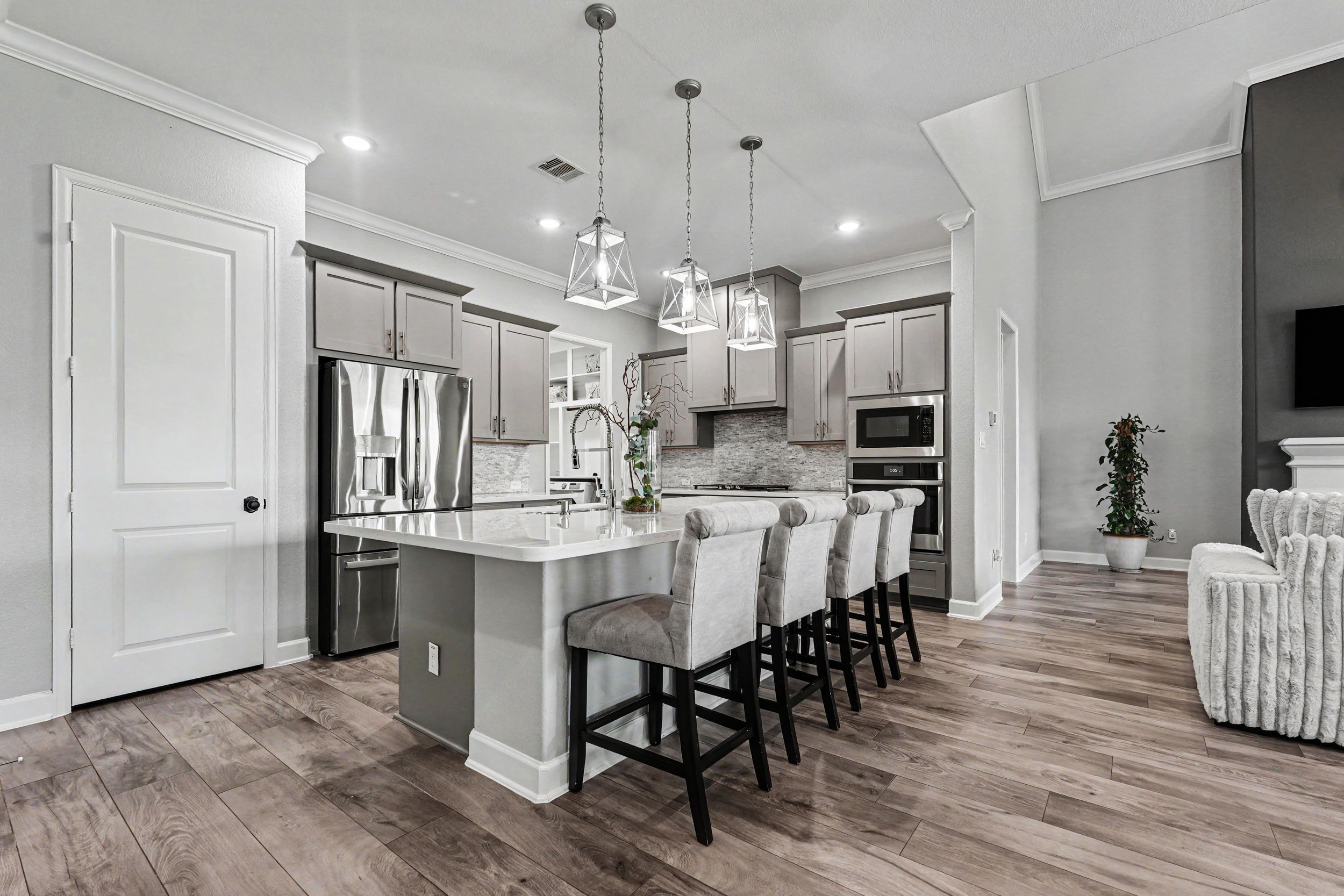 Modern gray kitchen with large island, bar seating, pendant lights, stainless appliances, and hardwood floors.