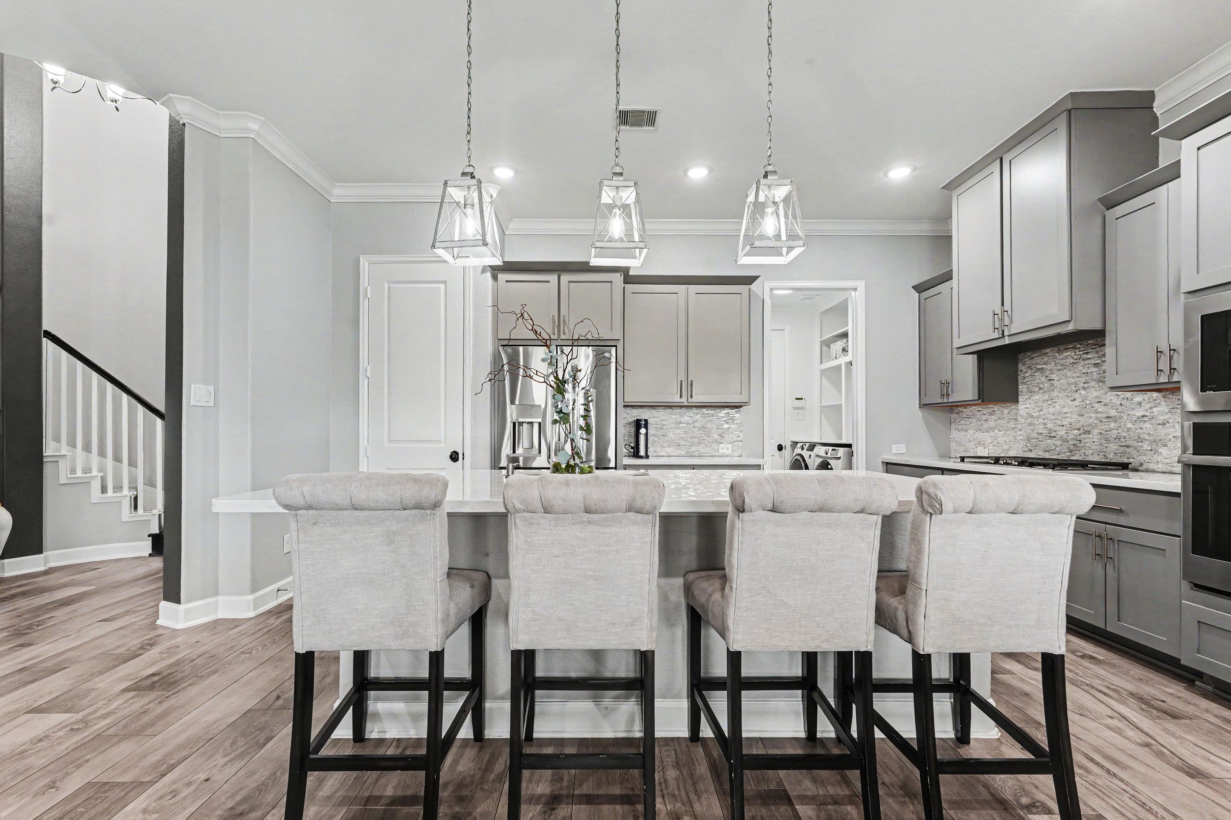 Modern kitchen with gray cabinets, marble island, velvet bar stools, and pendant lights over hardwood floors.
