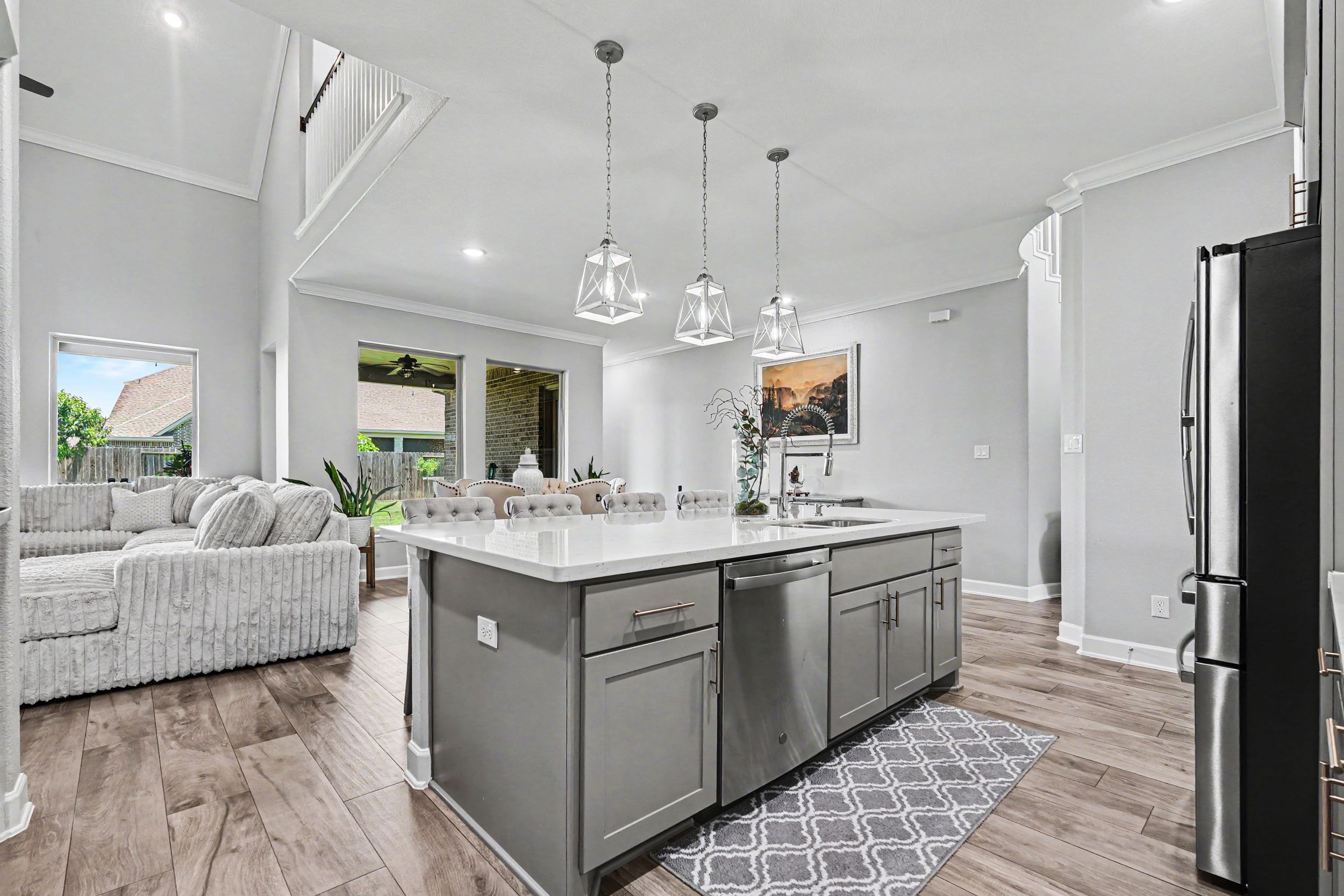 Open-concept kitchen with gray island, pendant lights, dishwasher, and view into living area with hardwood floors.