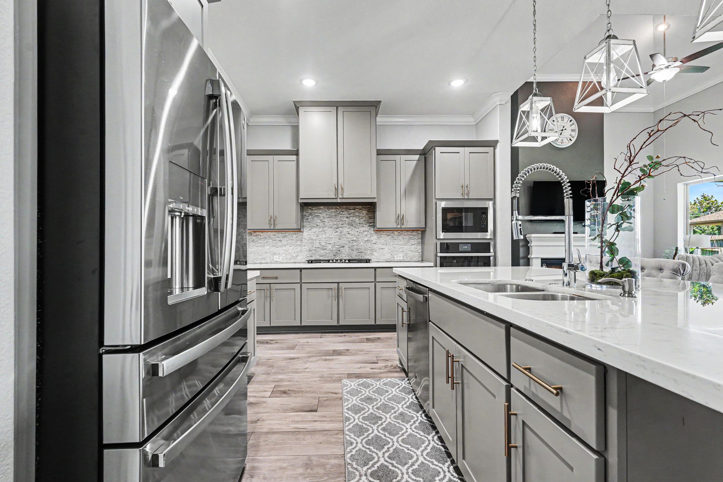 Modern kitchen with gray cabinets, stainless steel appliances, white quartz countertops, and hardwood floors.