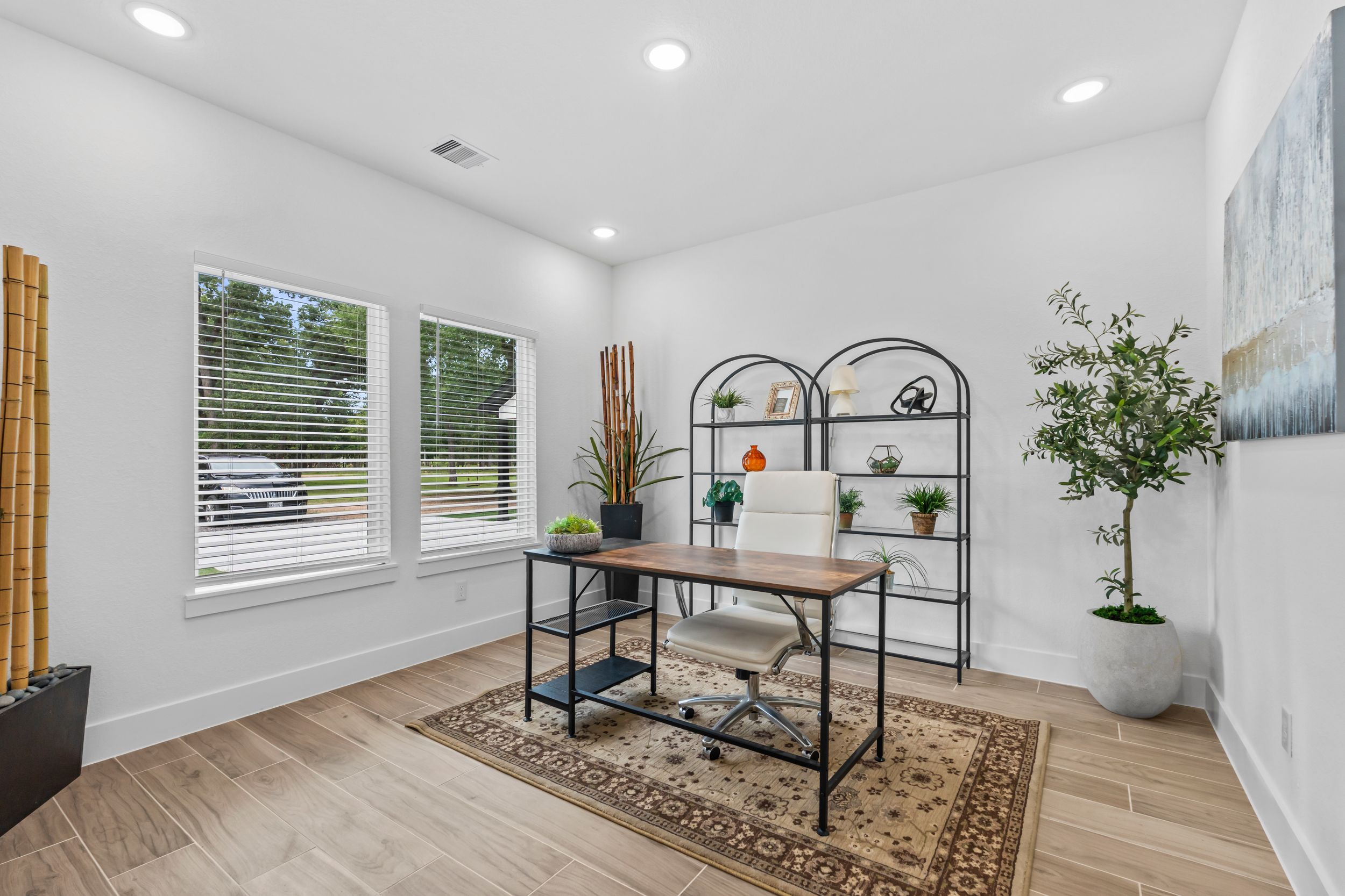 Bright home office with wood desk, arched metal shelves, hardwood floors, and large windows.