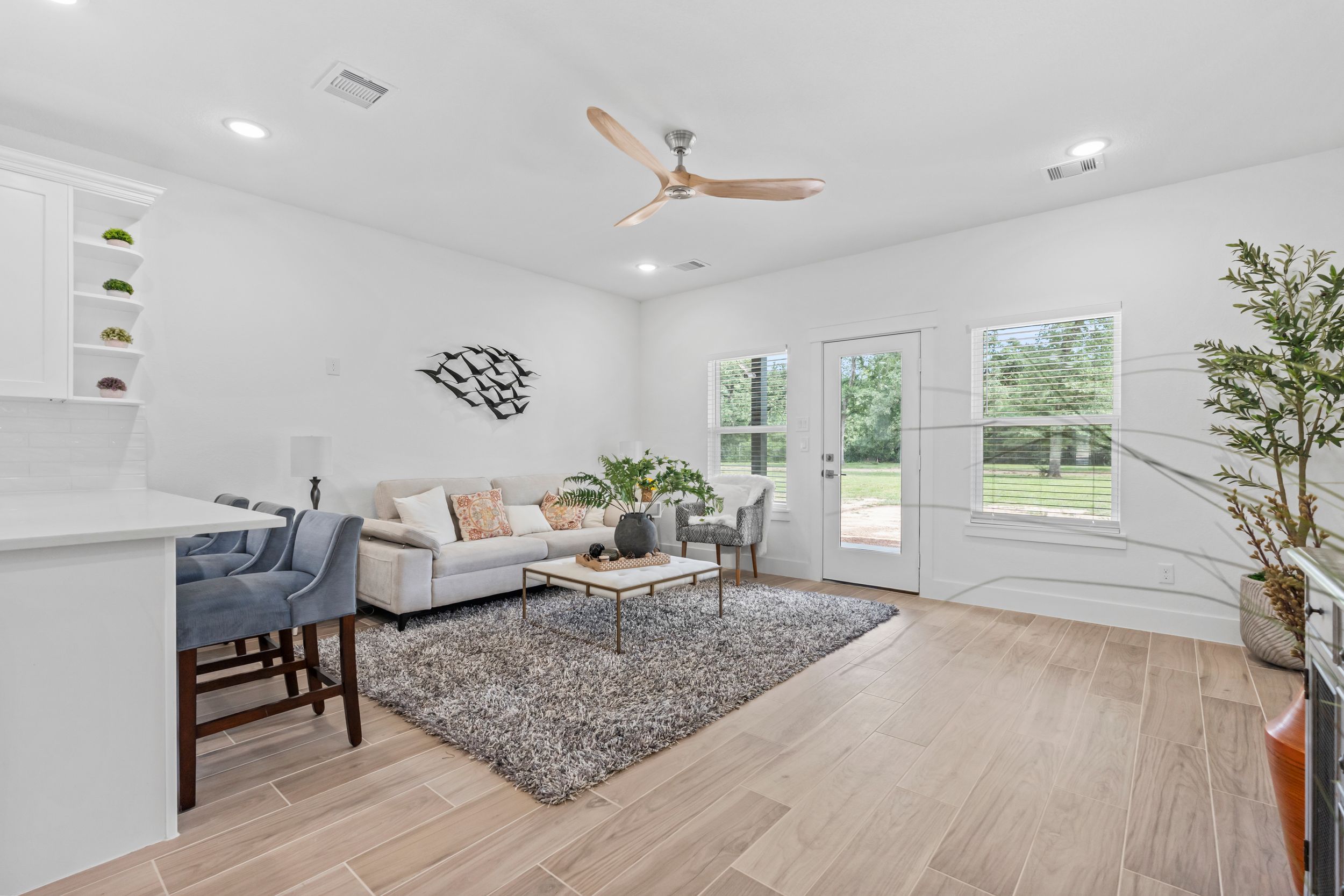 Spacious living room with ceiling fan, light hardwood floors, neutral sofa, and backyard views.
