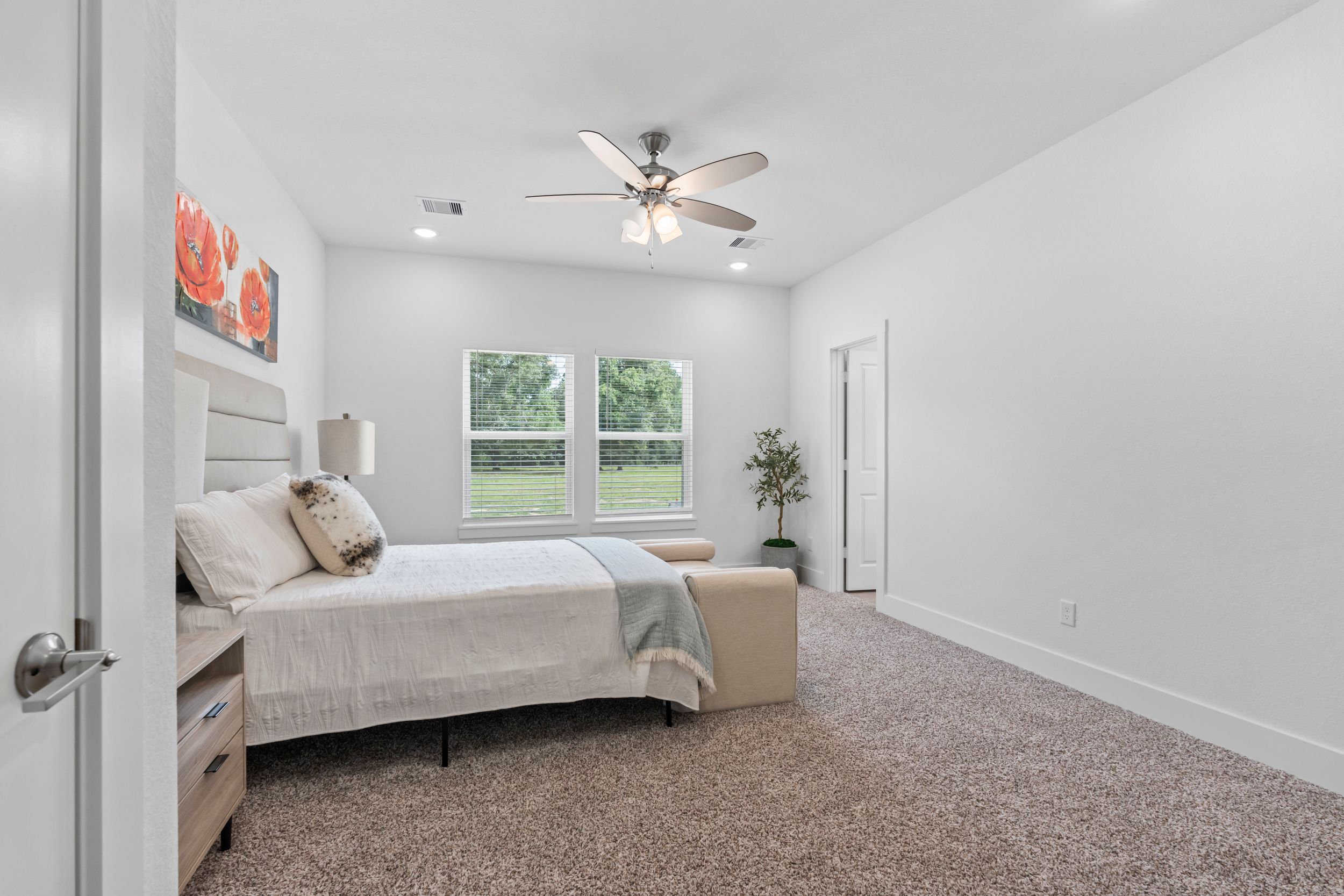 Bright bedroom with carpet, ceiling fan, natural light from window, and neutral decor in a modern home.