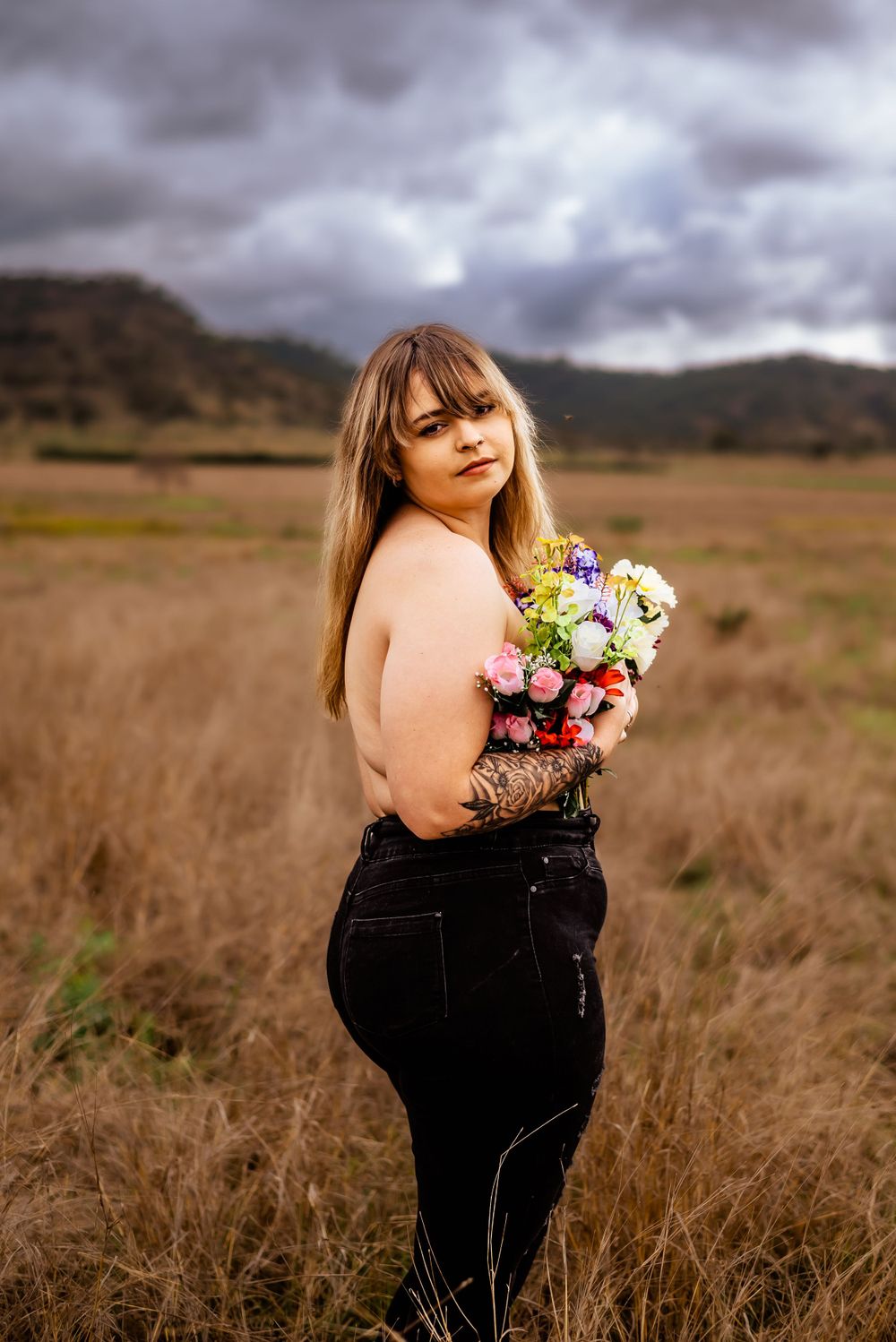 Artistic outdoor portrait with bouquet against dramatic mountain backdrop.
