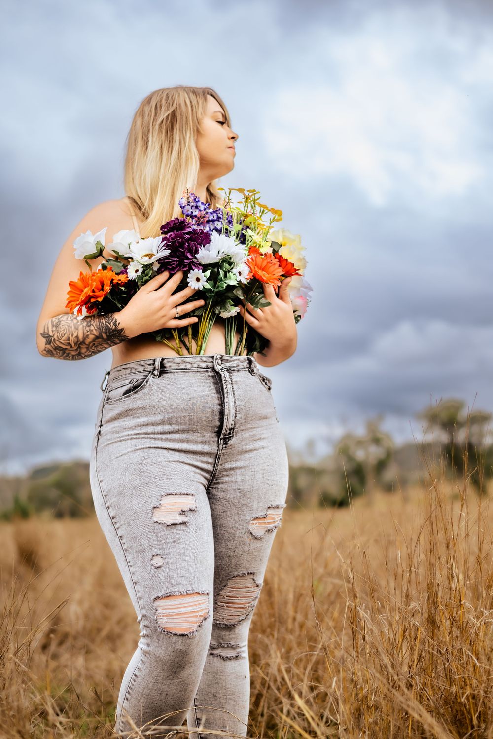 Figure embraces colorful bouquet while standing in sun-lit grassy field.