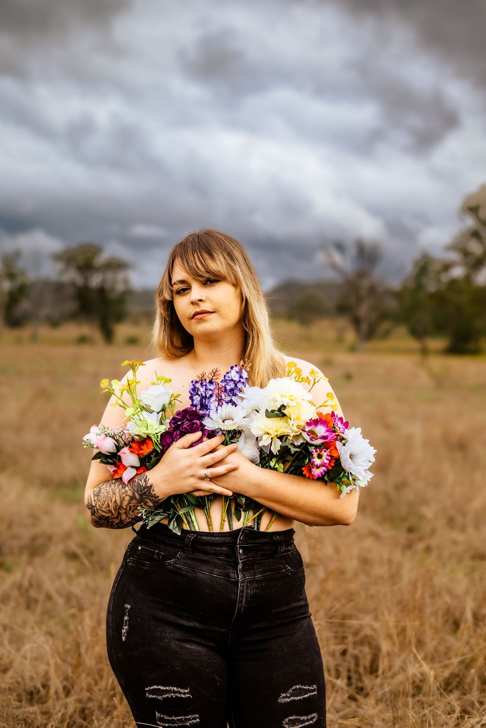 Colorful bouquet of flowers contrasts against moody sky and brown grass field.