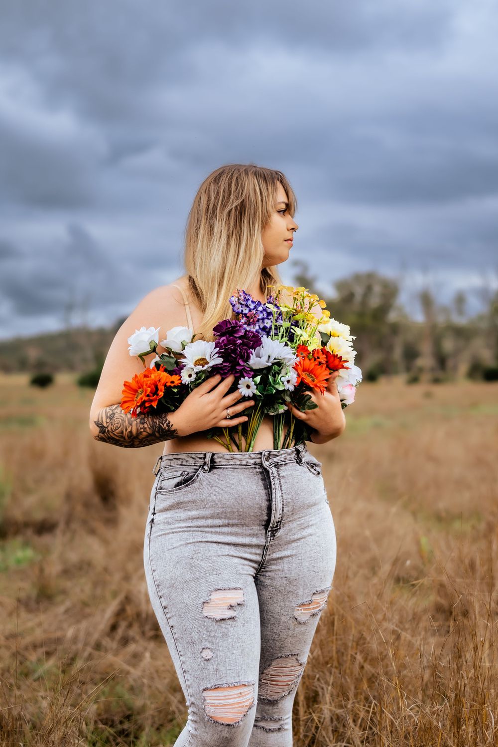 A colorful bouquet of wildflowers held against a moody sky in an open field setting.