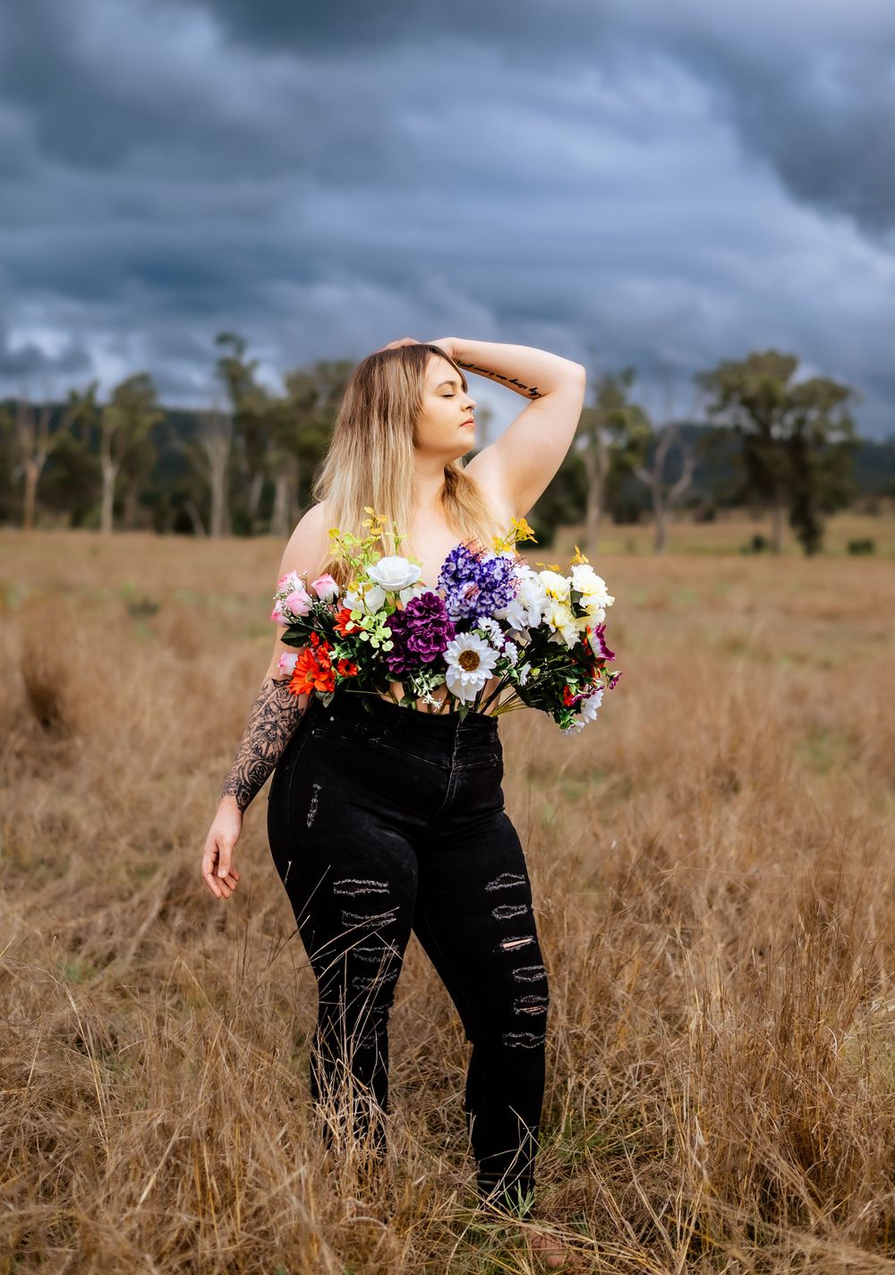 Dramatic outdoor portrait with colorful flowers against stormy countryside.