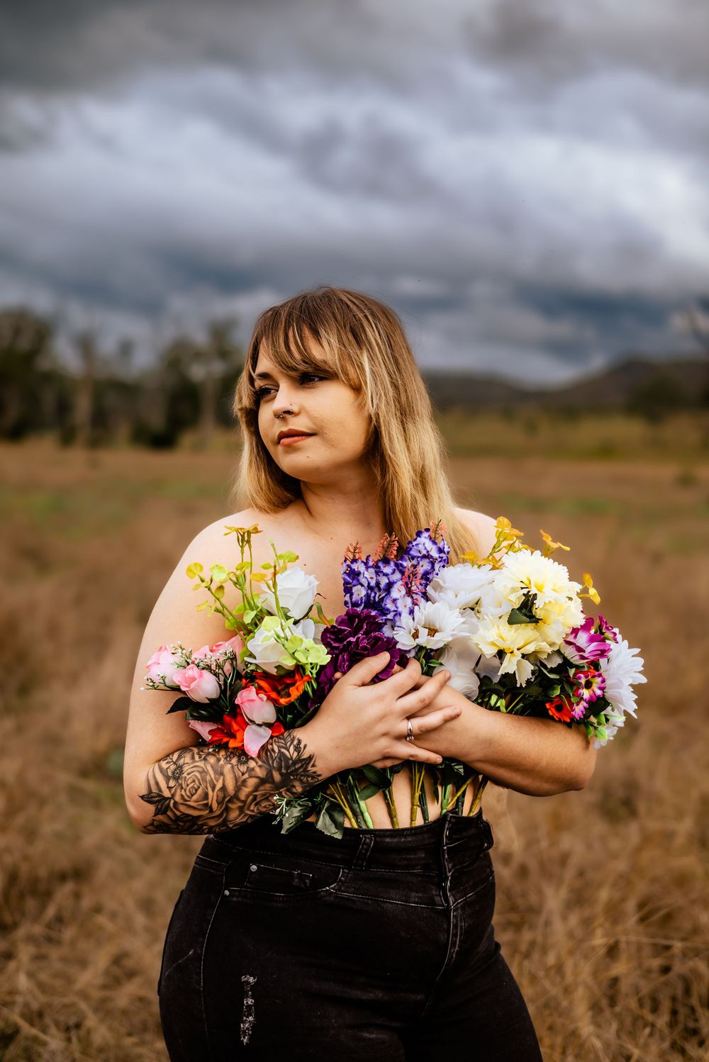 Person holding colorful bouquet of fresh flowers in rustic field setting.