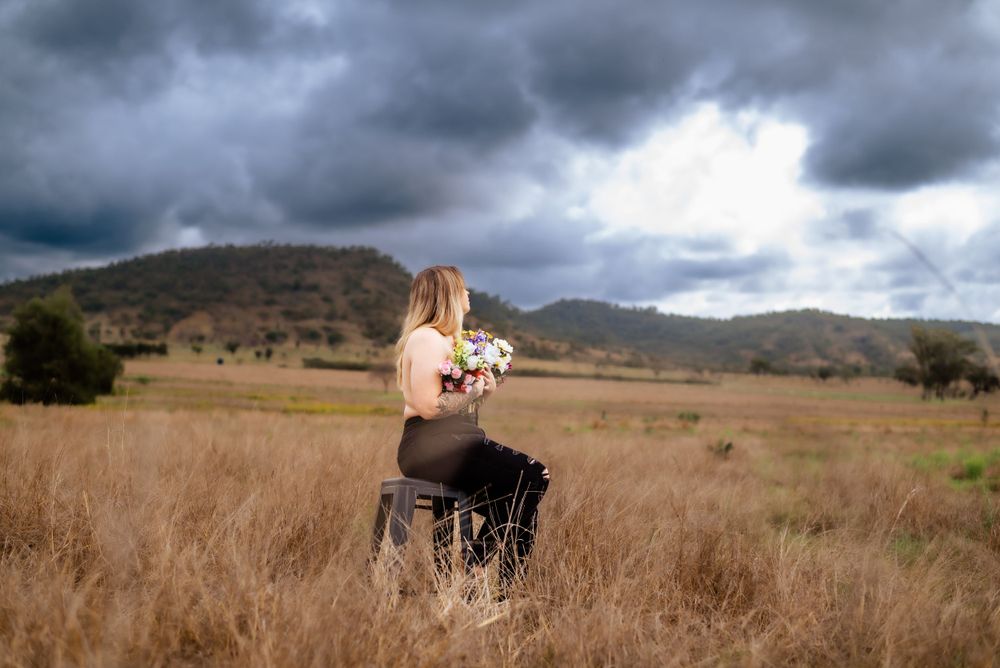 Figure sitting in tall grass field with stormy mountain landscape in background.