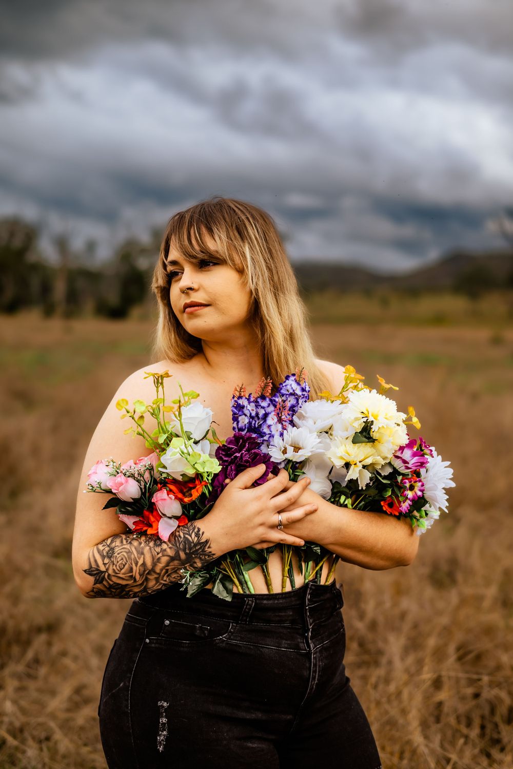 Light illuminates subject holding bright floral arrangement in rustic field setting.