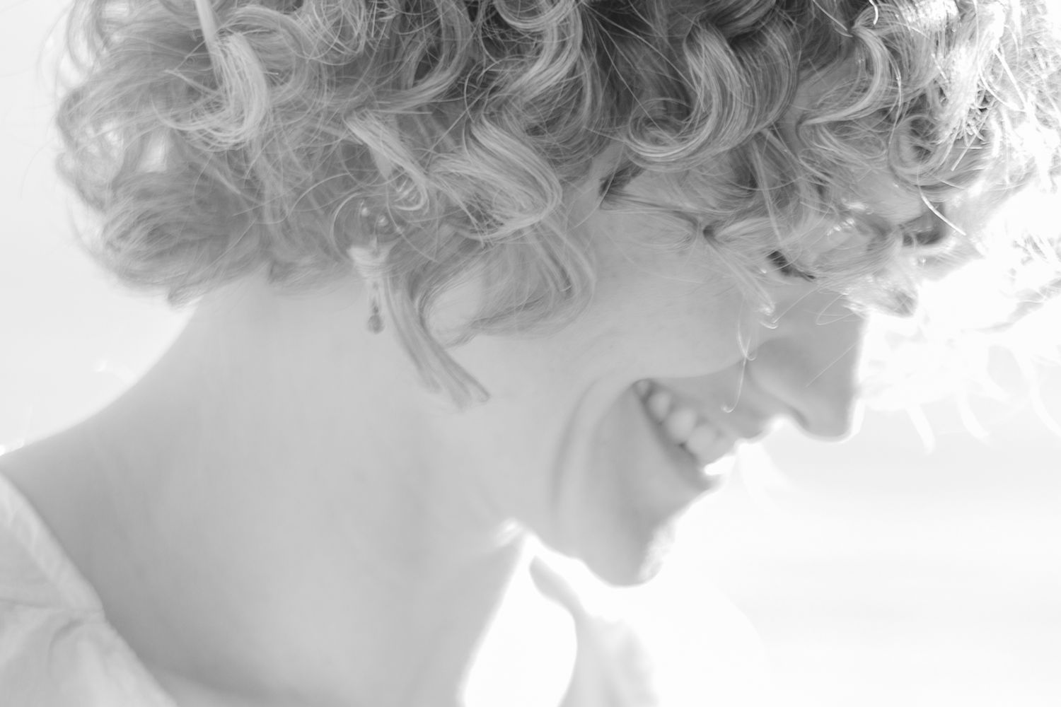 Side profile portrait showing curly hair and natural smile in soft black and white.
