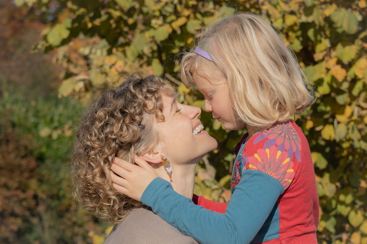 Tender outdoor moment captured between parent and child against autumn foliage.