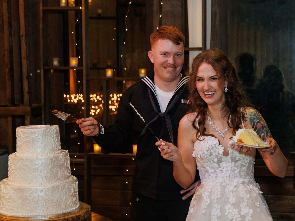 Bride and groom in Navy uniform cutting their white tiered wedding cake at a rustic reception venue.