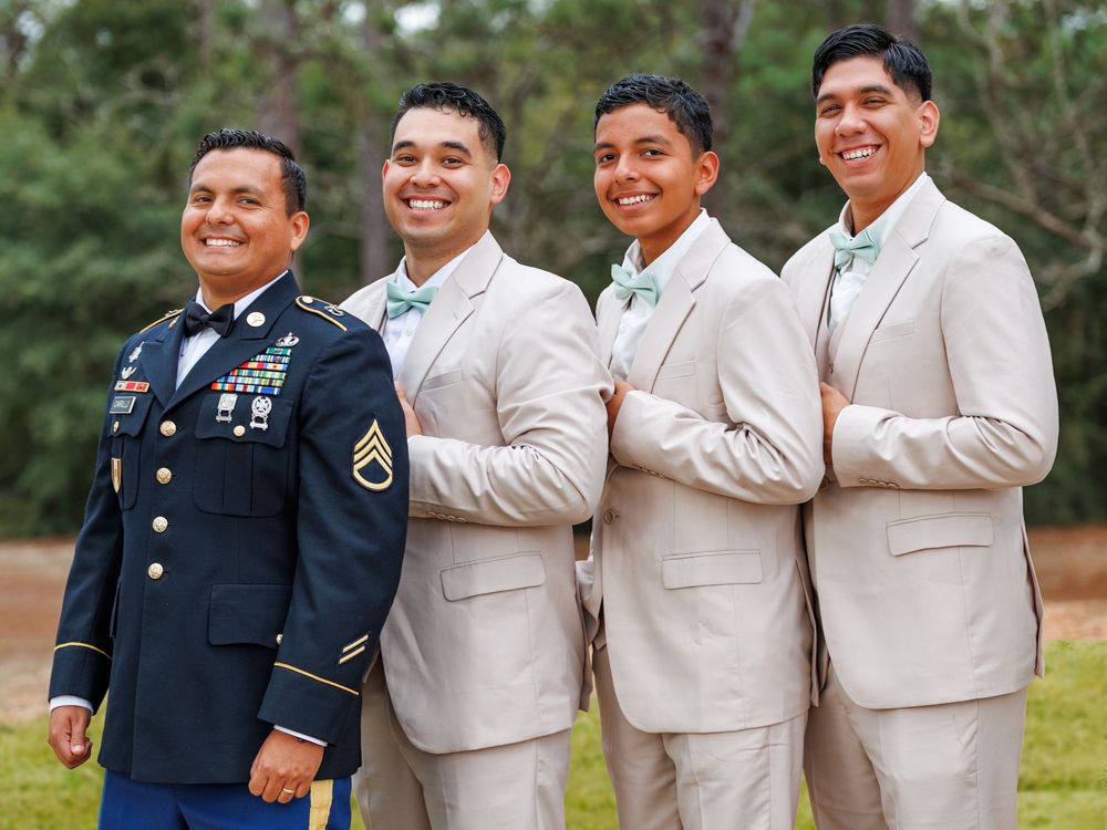 A group in tan suits and military dress uniforms pose together outdoors for formal photos.