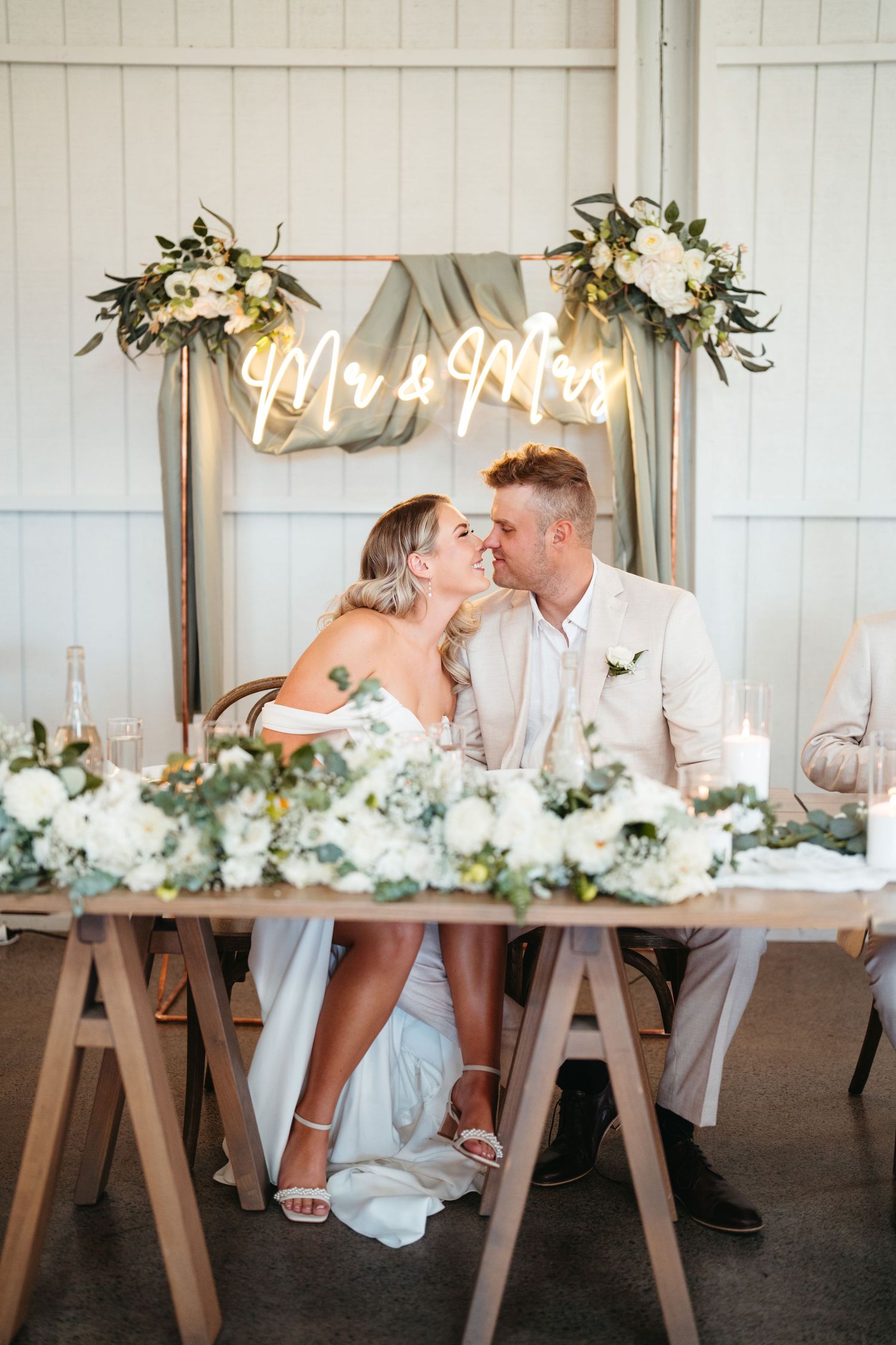 A couple shares an intimate moment at their reception table under a neon Mr & Mrs sign at The Hunting Lodge wedding venue in Auckland.