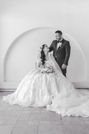 Black and white portrait of couple in wedding attire posed in arched architectural setting.