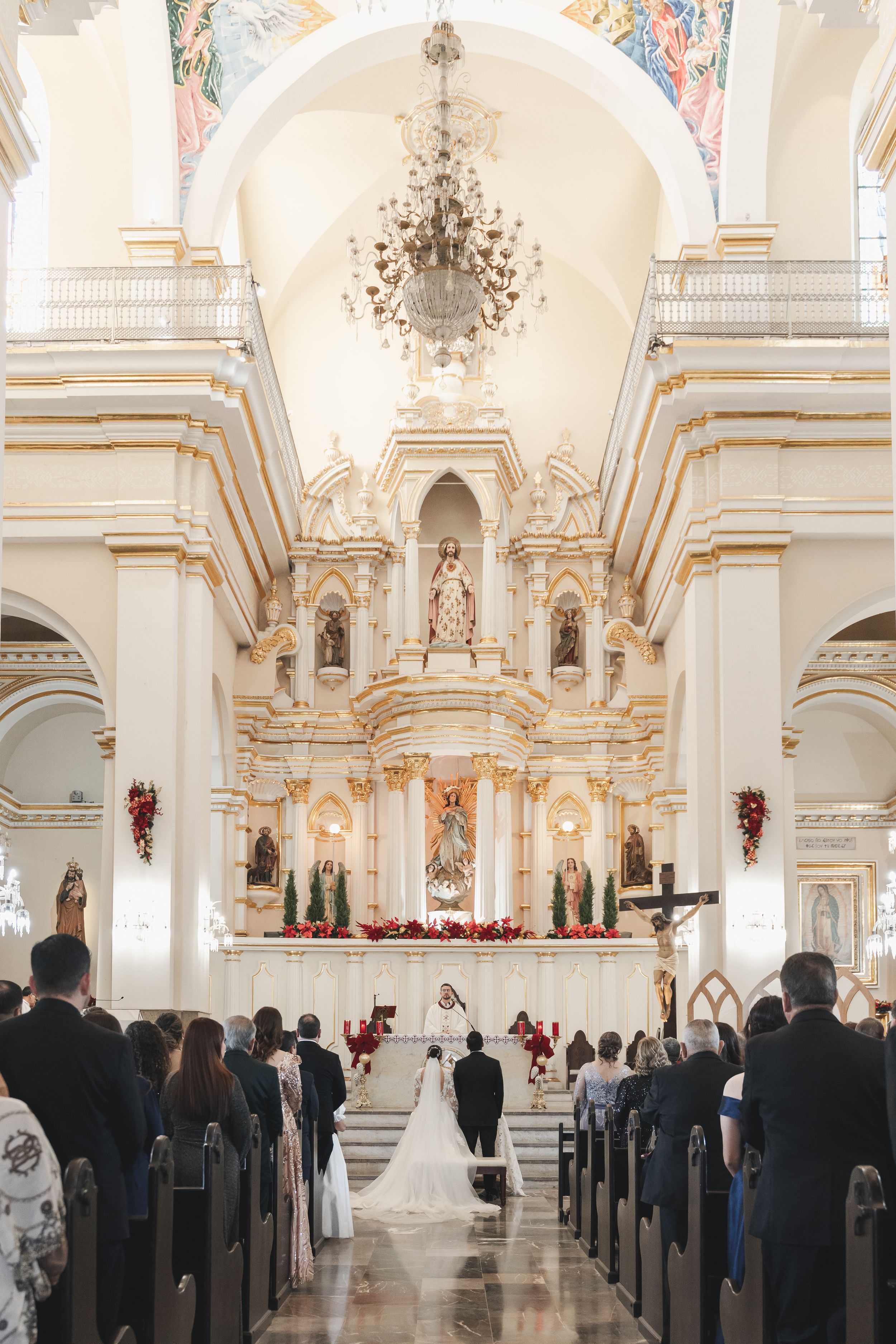 Ornate white church interior with baroque details and crystal chandeliers during wedding ceremony.