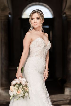 Bride in a detailed lace wedding gown holds a delicate bouquet in an elegant venue.