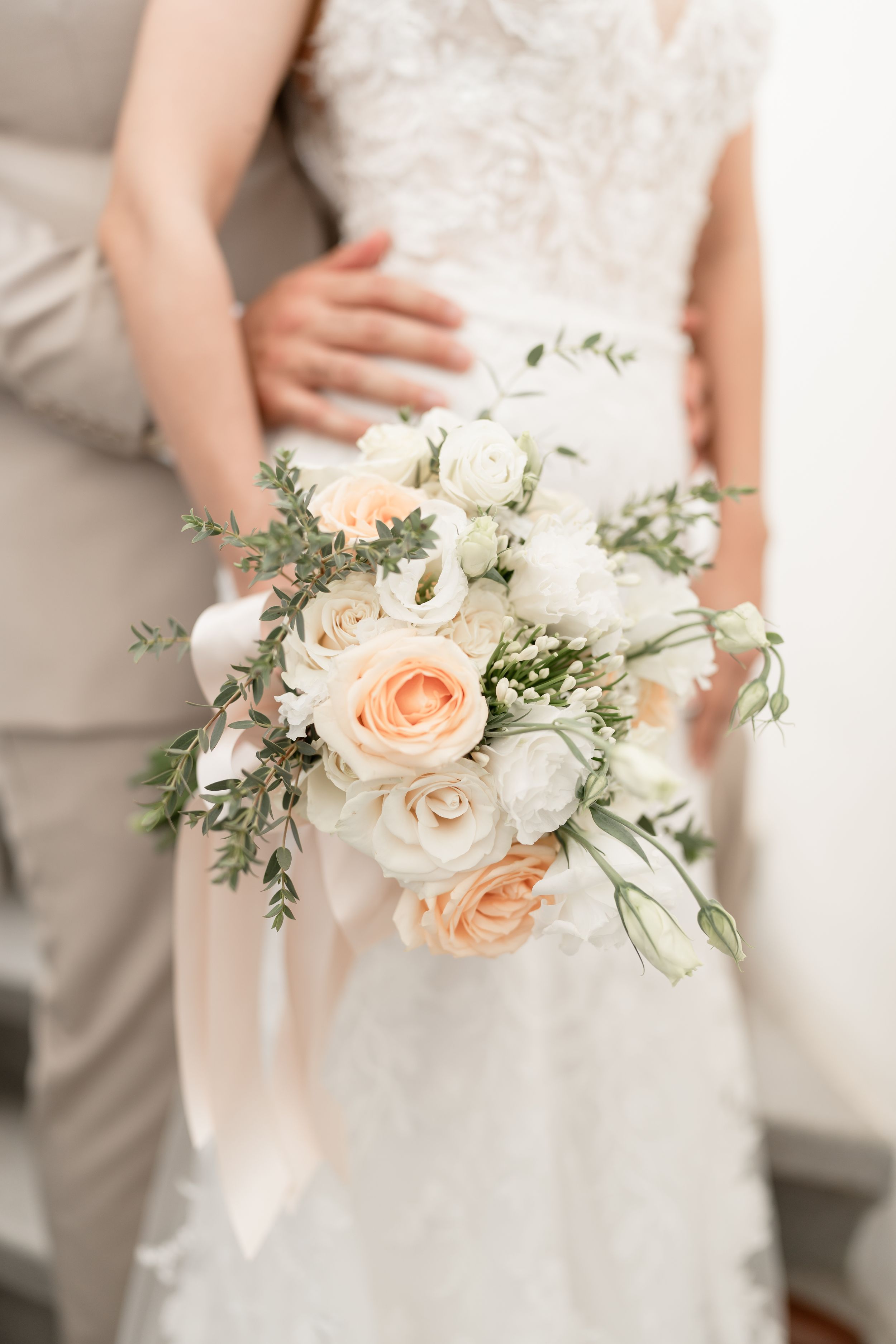 Elegant bridal bouquet featuring peach and white roses with greenery against a white wedding dress.