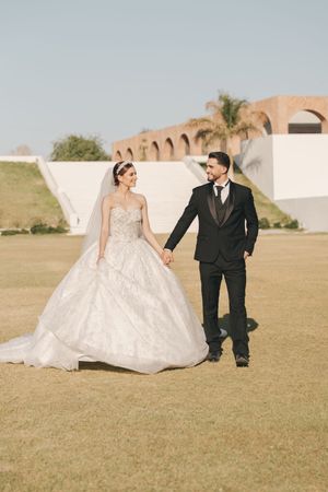 A couple in wedding attire poses playfully on a grassy field during their outdoor photo session.