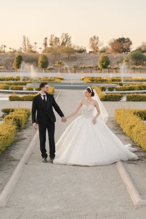 Wedding couple walking and posing in landscaped garden with fountain and hedges.
