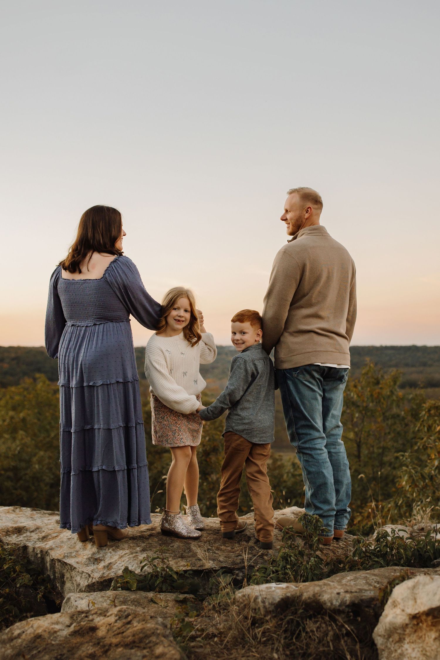 Family stands together on rocky overlook enjoying scenic autumn mountain view at sunset.
