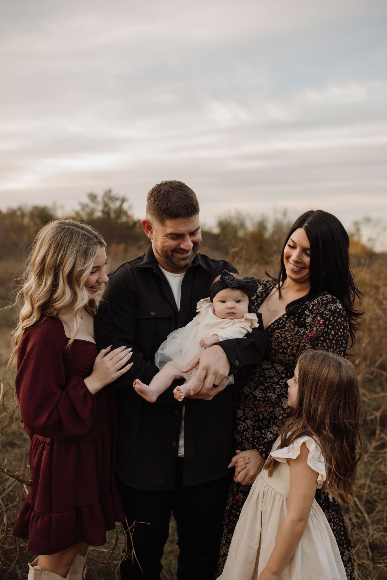 Family shares tender moments together outdoors during sunset photo session in a natural field setting.