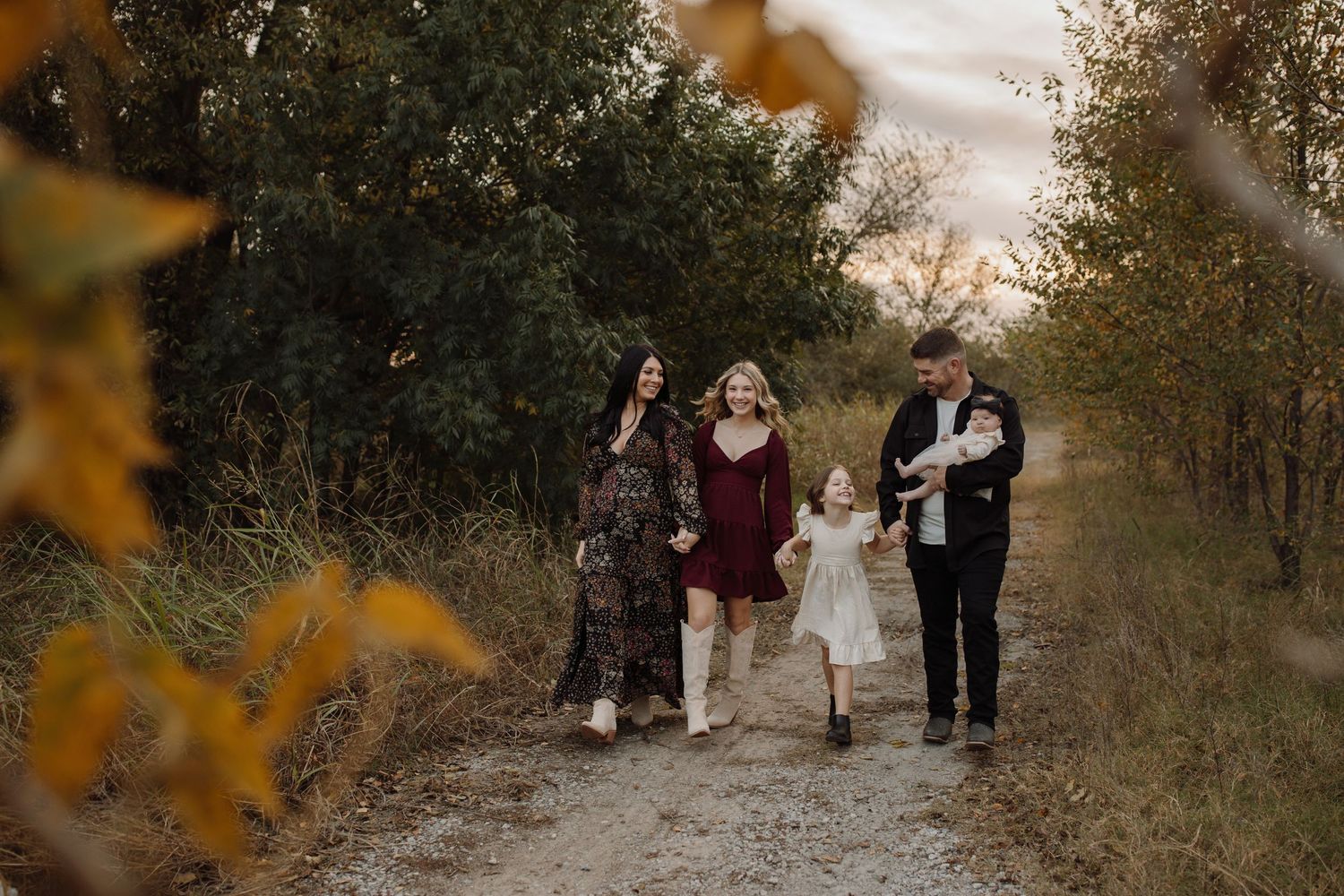 A group walks together down a rustic dirt path surrounded by autumn foliage on a cloudy day.