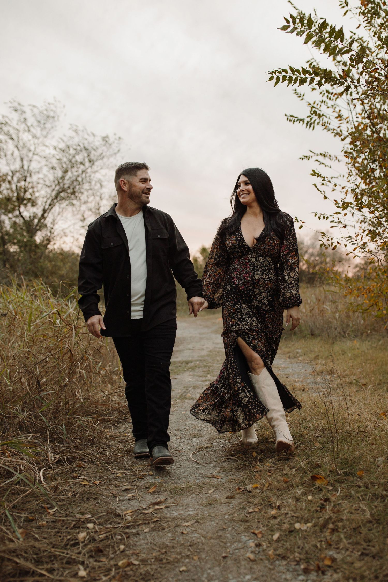 A couple walks together and shares intimate moments in a natural autumn setting with dried grass and foliage.