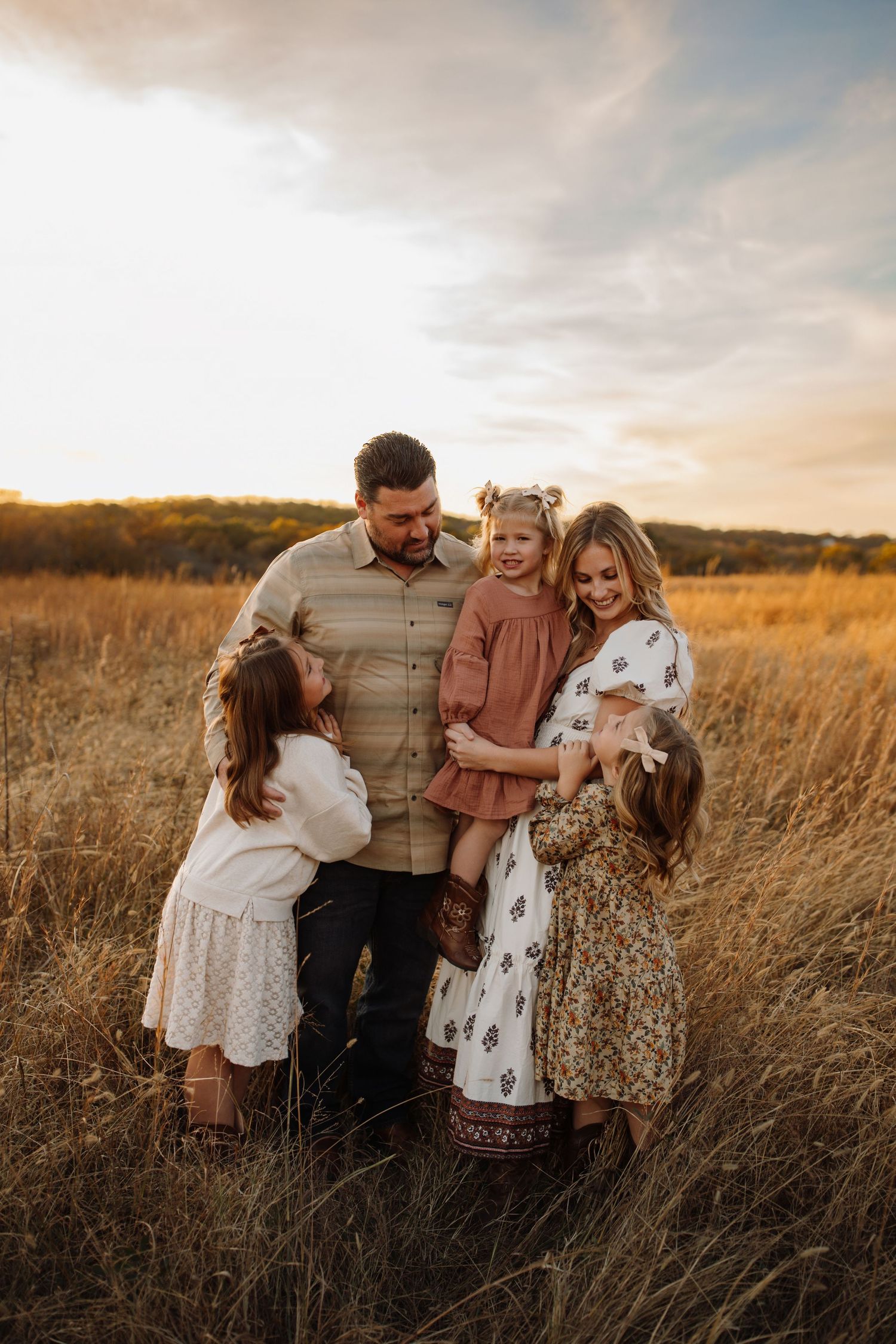 A family shares a tender moment together in a golden autumn field at sunset.