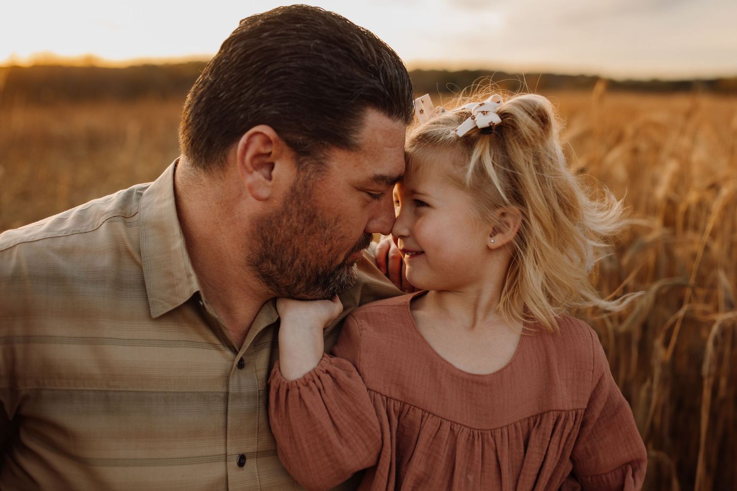 A romantic couple embraces in a golden wheat field at sunset creating an intimate outdoor portrait.