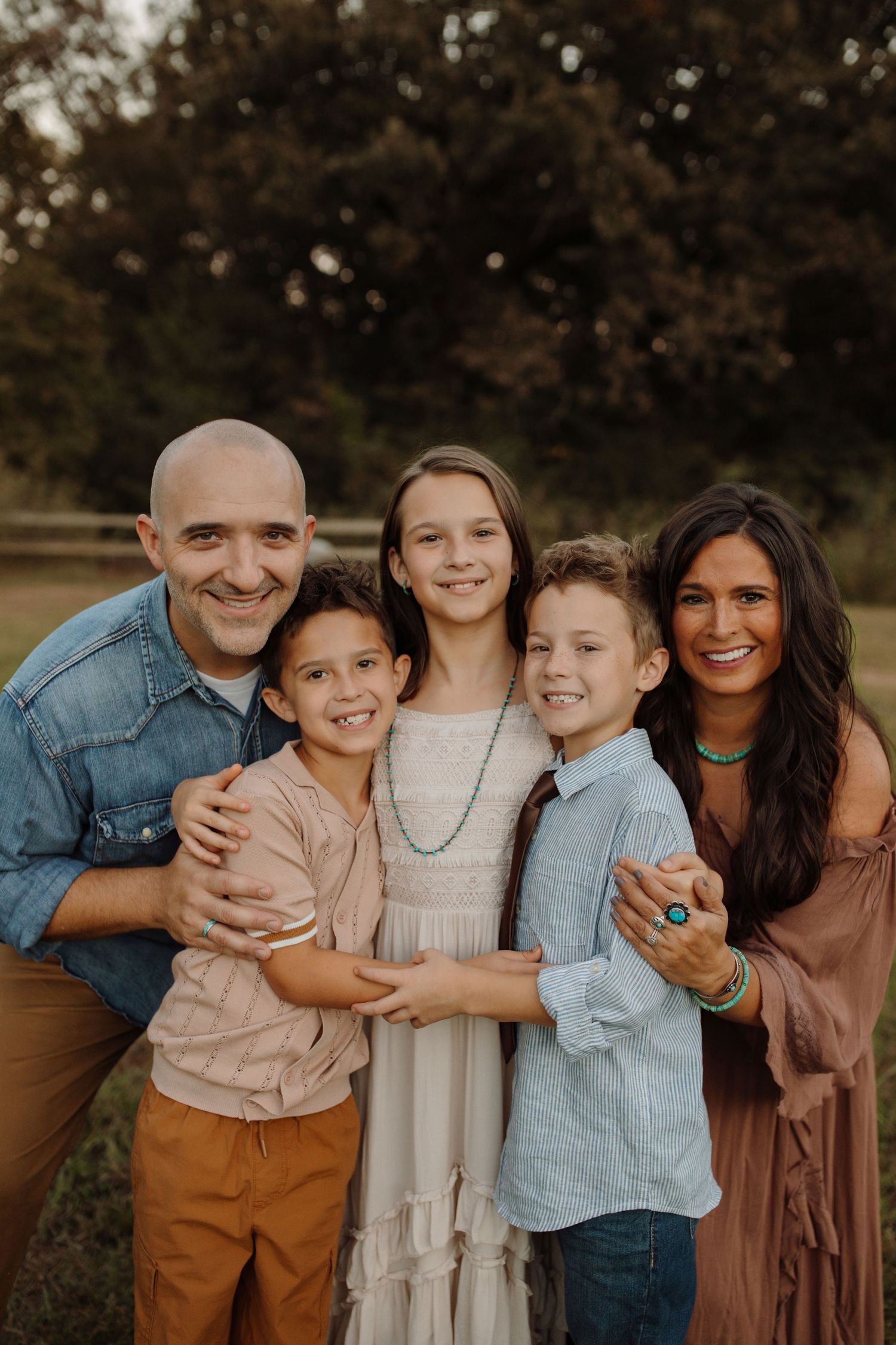 A family of five poses together outdoors in coordinated casual outfits during a sunset photo session.