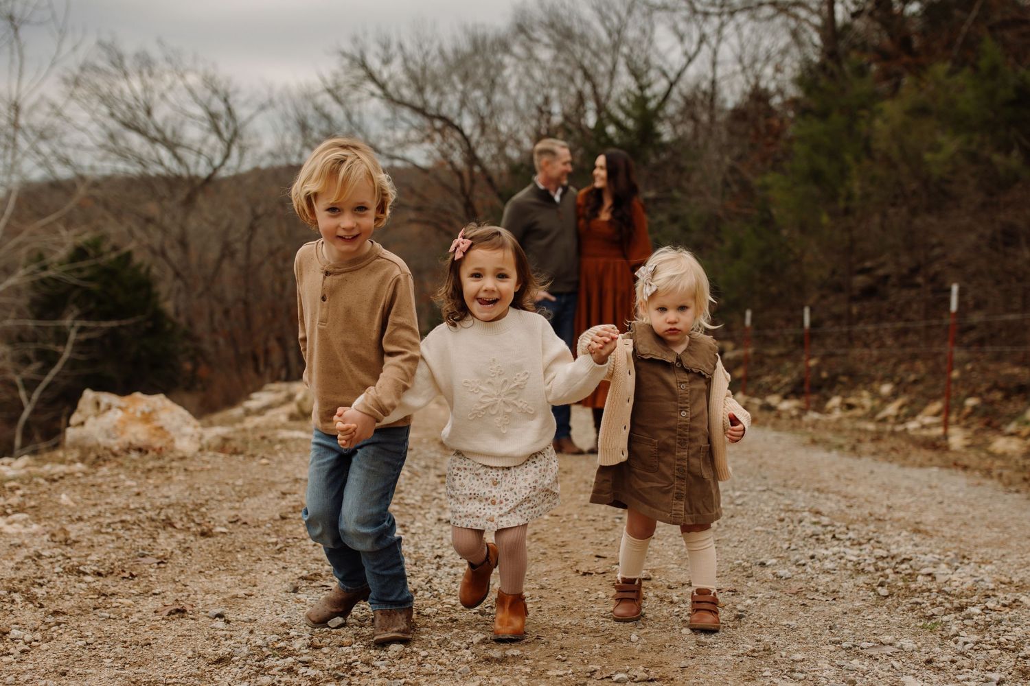 A family in earth-toned clothing walks together on a rocky path during an autumn outdoor photo session.