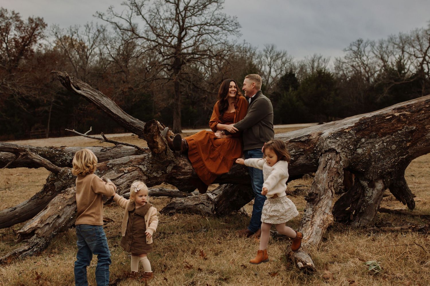 A group of people dance and twirl together in a rustic outdoor setting at sunset with tall grass and trees.