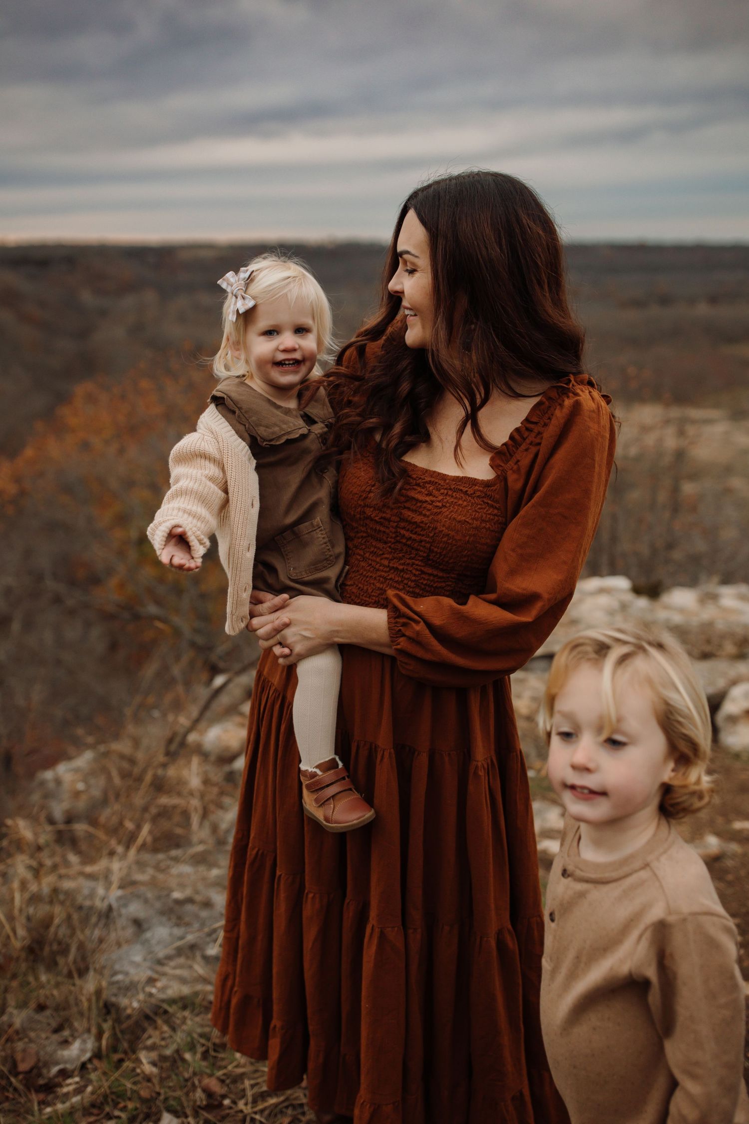 A family wearing coordinating brown and beige outfits shares joyful moments against a desert landscape backdrop.