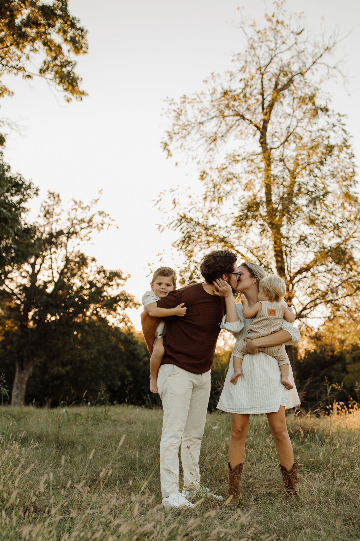 Family members embrace in a golden field during sunset with trees in the background.