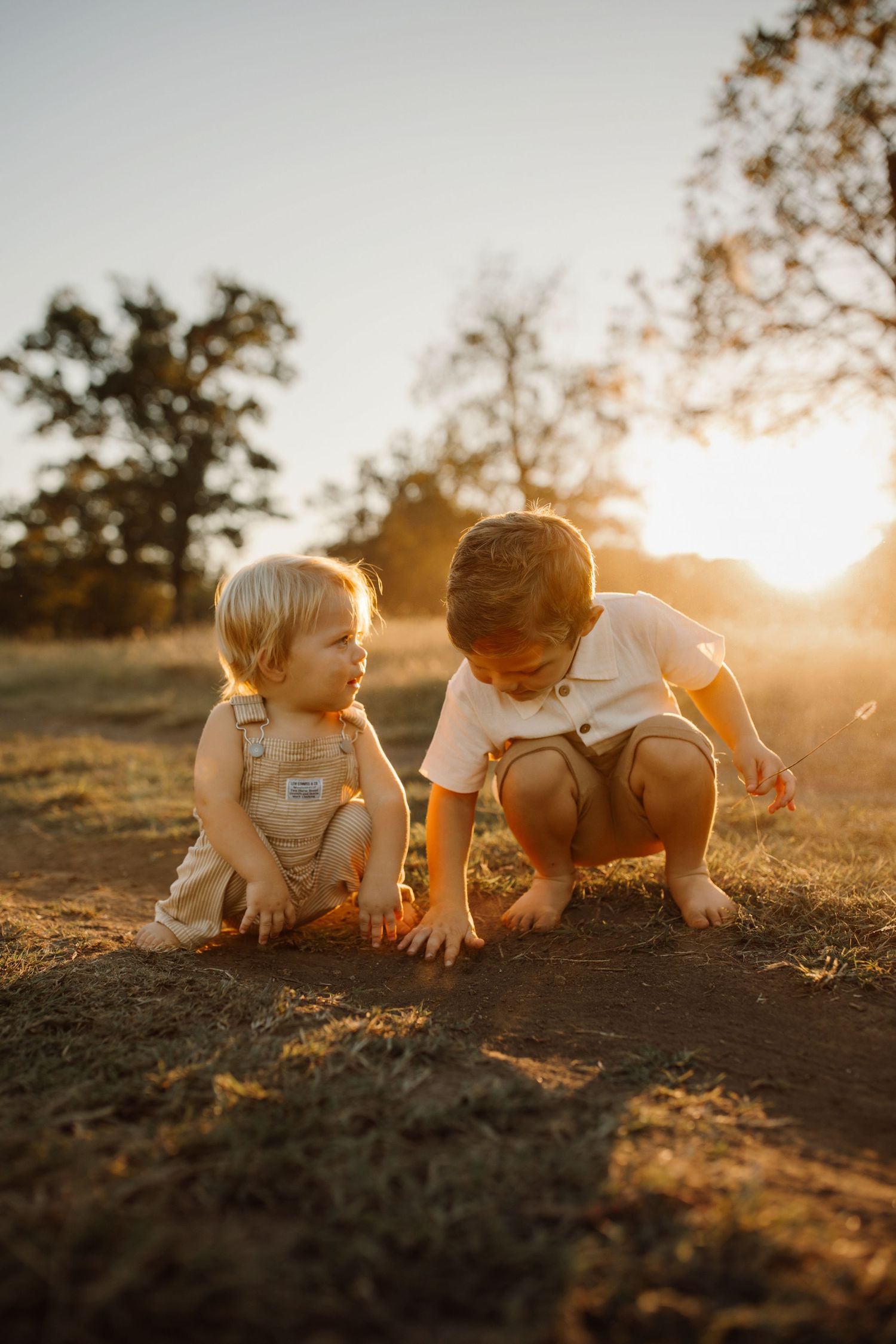 Children explore and play in the dirt together during golden hour sunset as warm sunlight illuminates the scene.