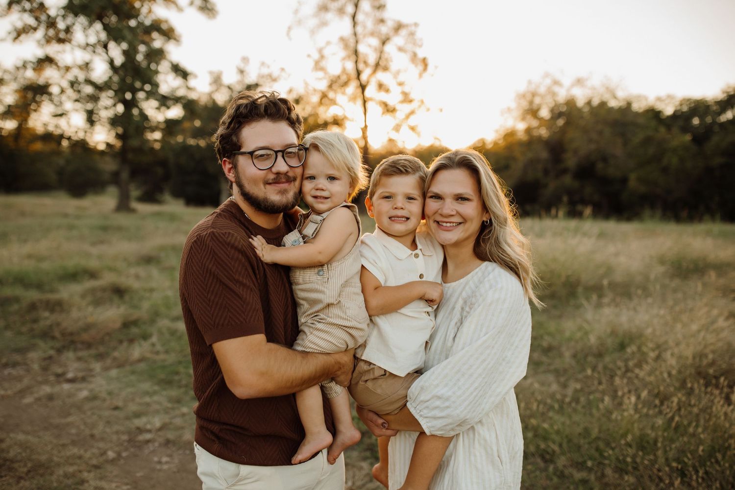 A family shares tender moments together in a sunlit meadow during golden hour photography session.