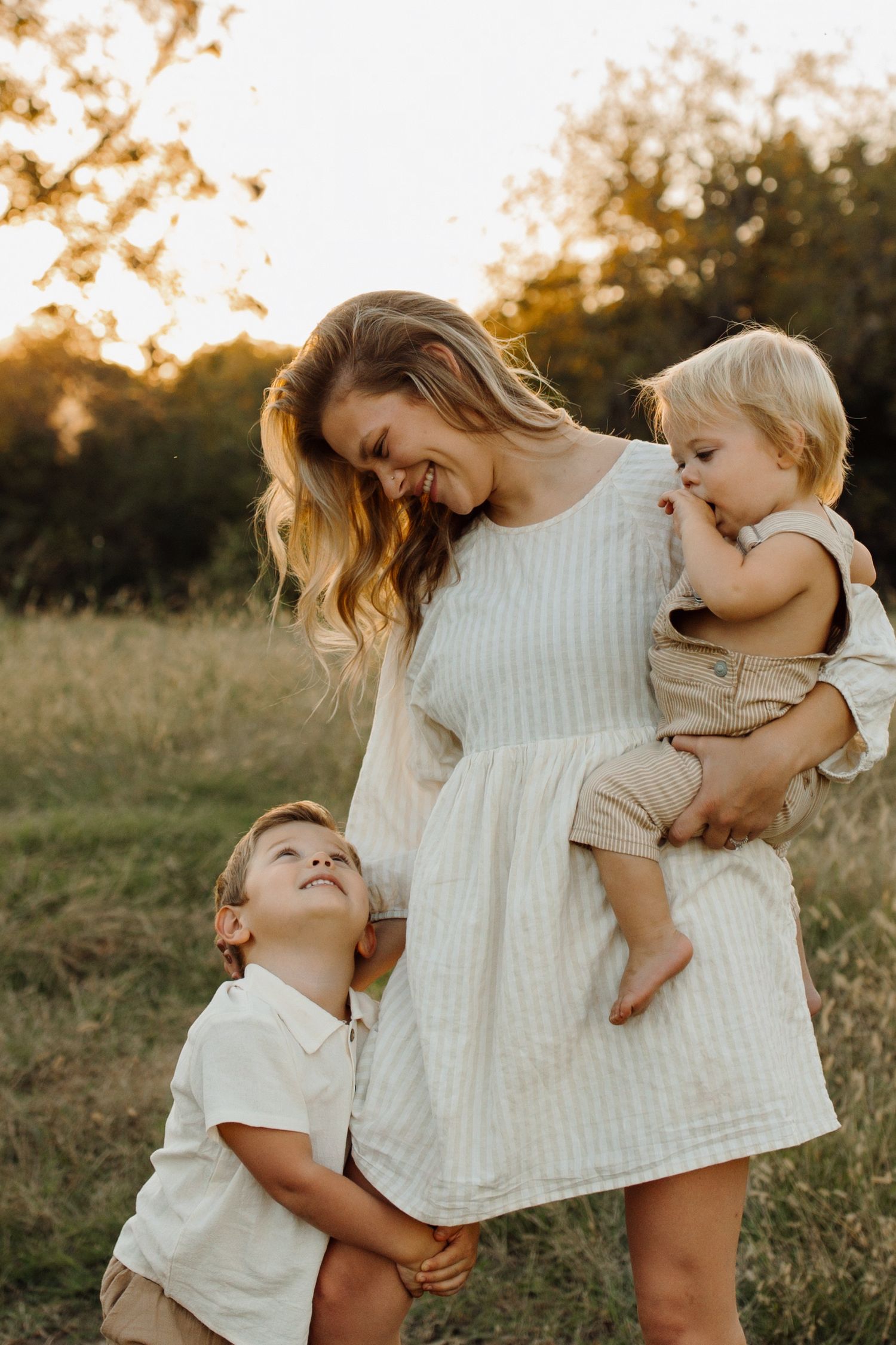 A tender family moment captured in a golden field at sunset with warm natural lighting and neutral earth-toned clothing.