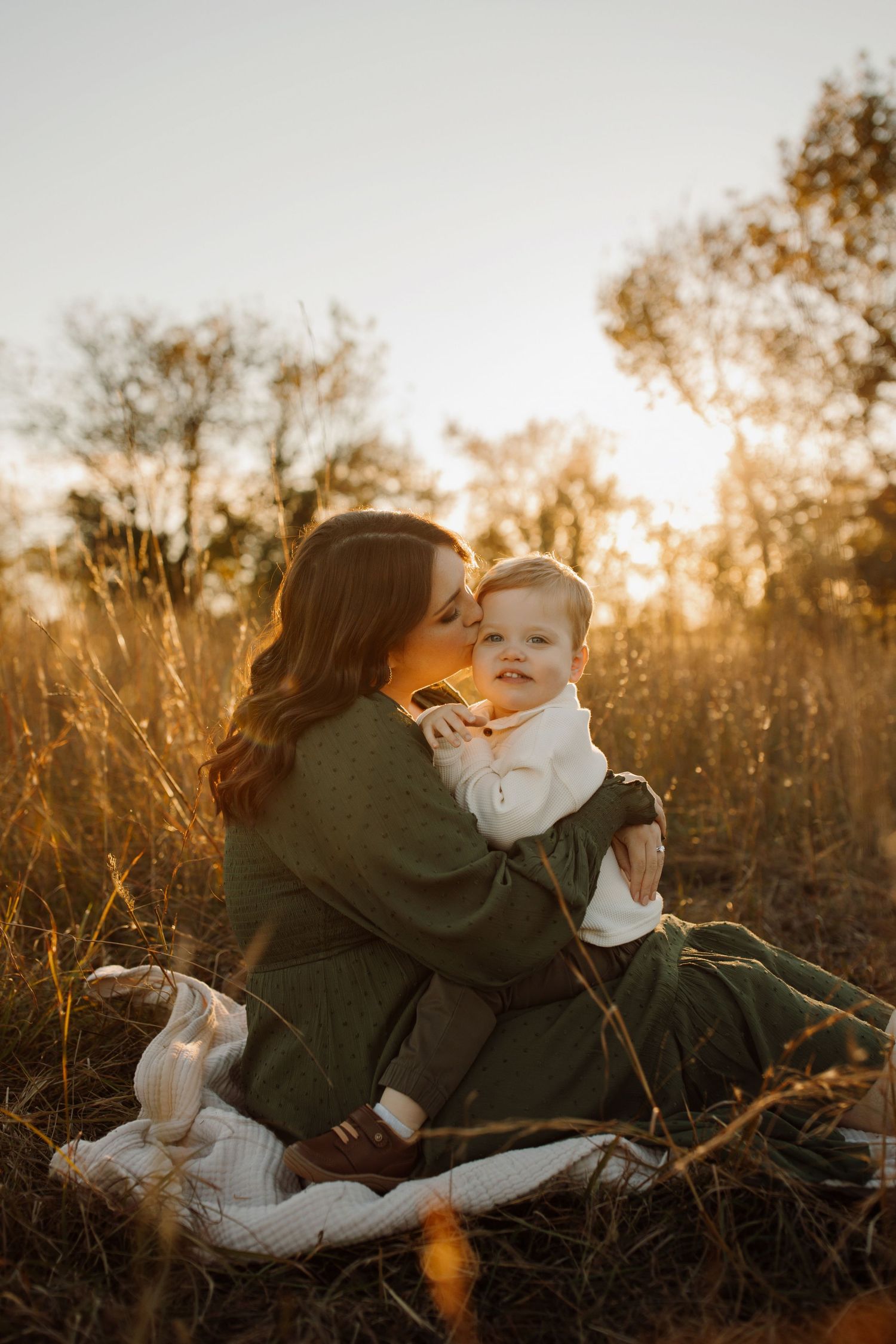 A tender family moment captured at sunset in a field of tall grass with warm golden light filtering through.
