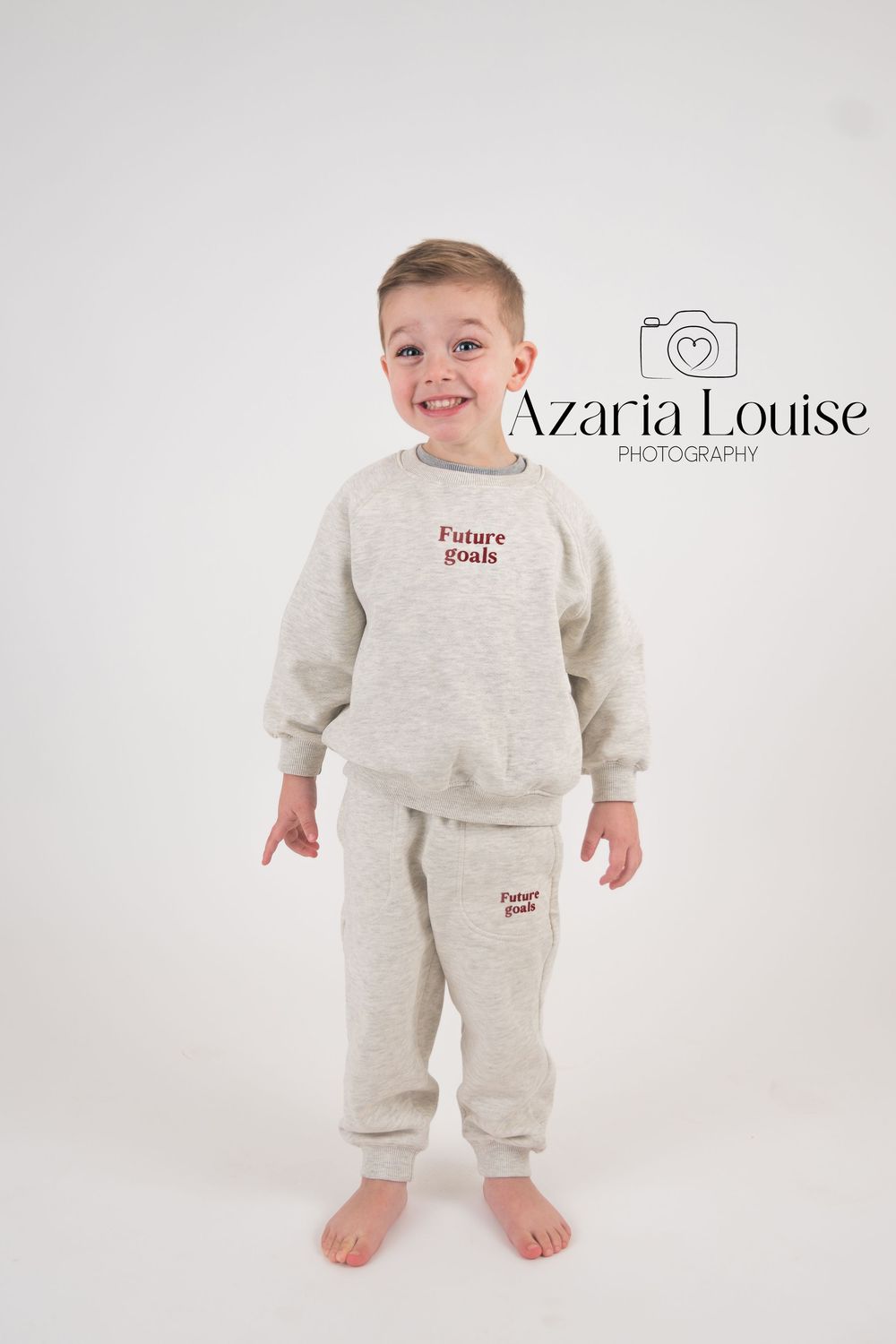 Professional studio portrait of a child wearing a cozy light gray sweatsuit against a white backdrop.