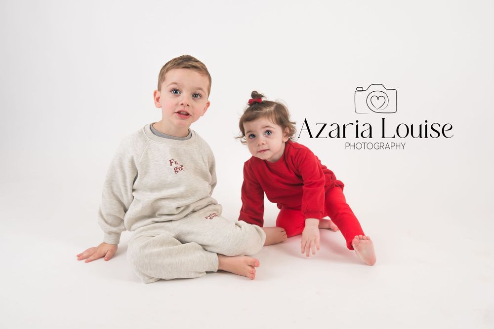 Two young children in matching holiday pajamas pose together on a white backdrop for Azaria Louise Photography.