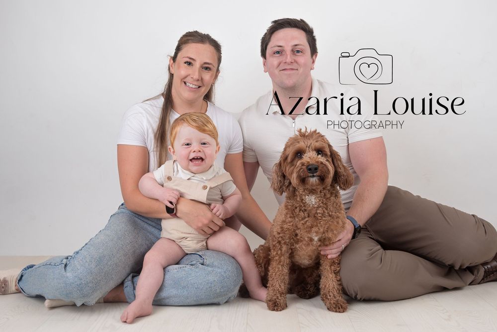 Professional family portrait with a baby and goldendoodle dog against a white studio background.