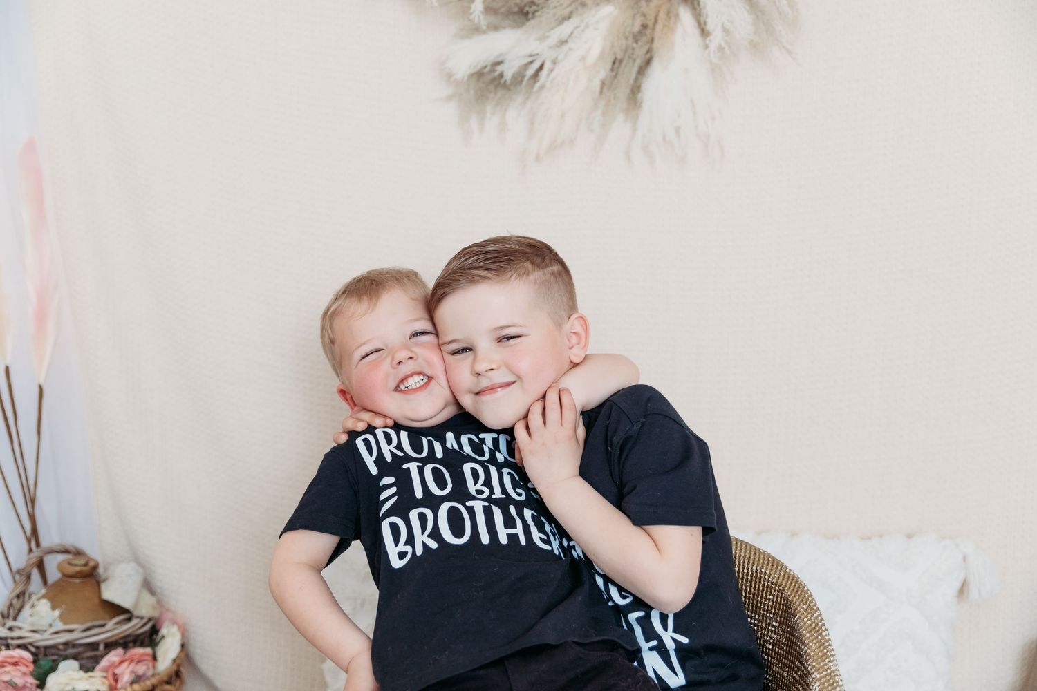 Two young boys in black shirts embracing and smiling against white wall. Photographer. Hull. East Yorkshire. Photography
