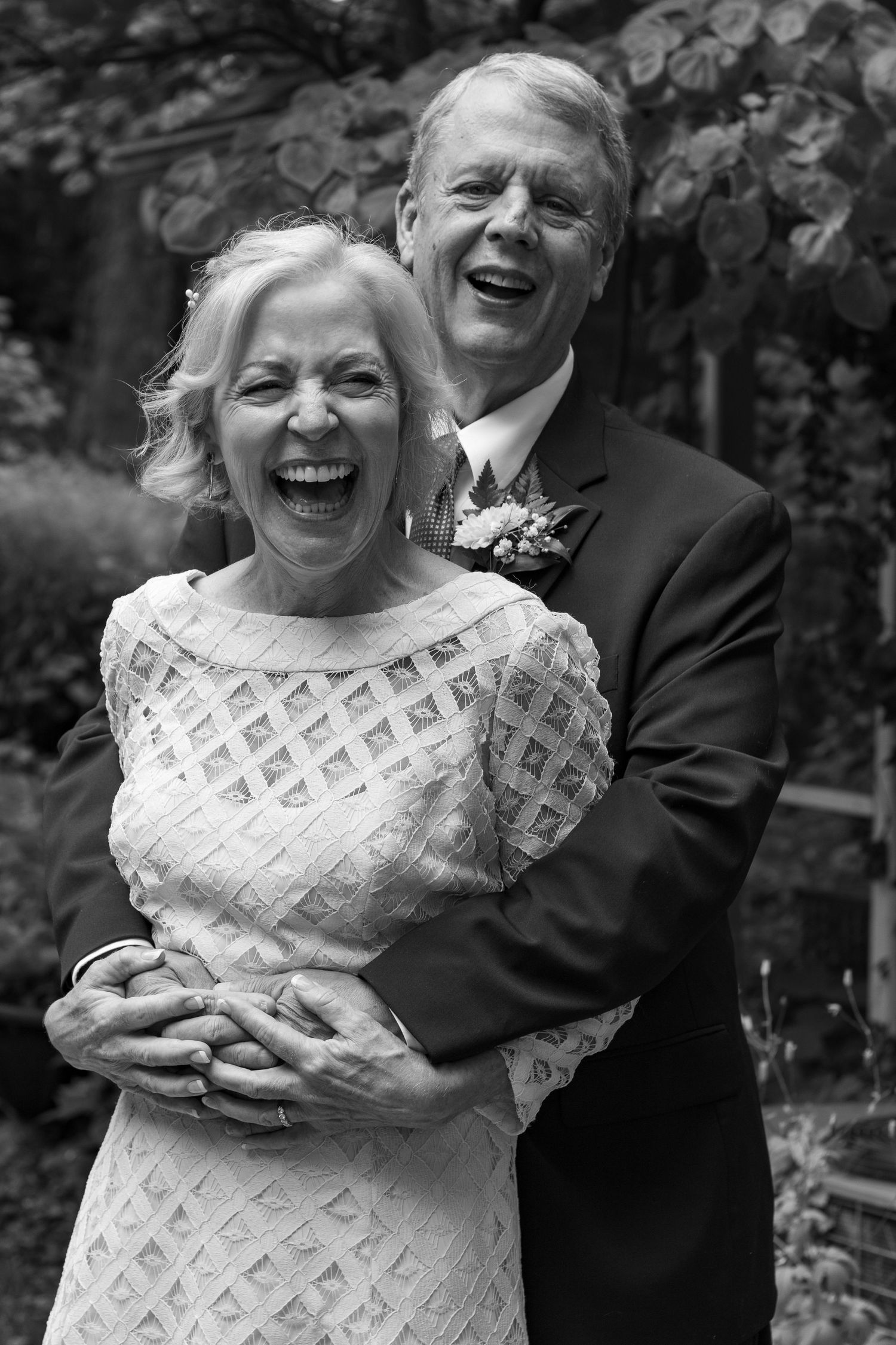 A couple shares joyful laughter together while embracing outdoors in black and white photography.