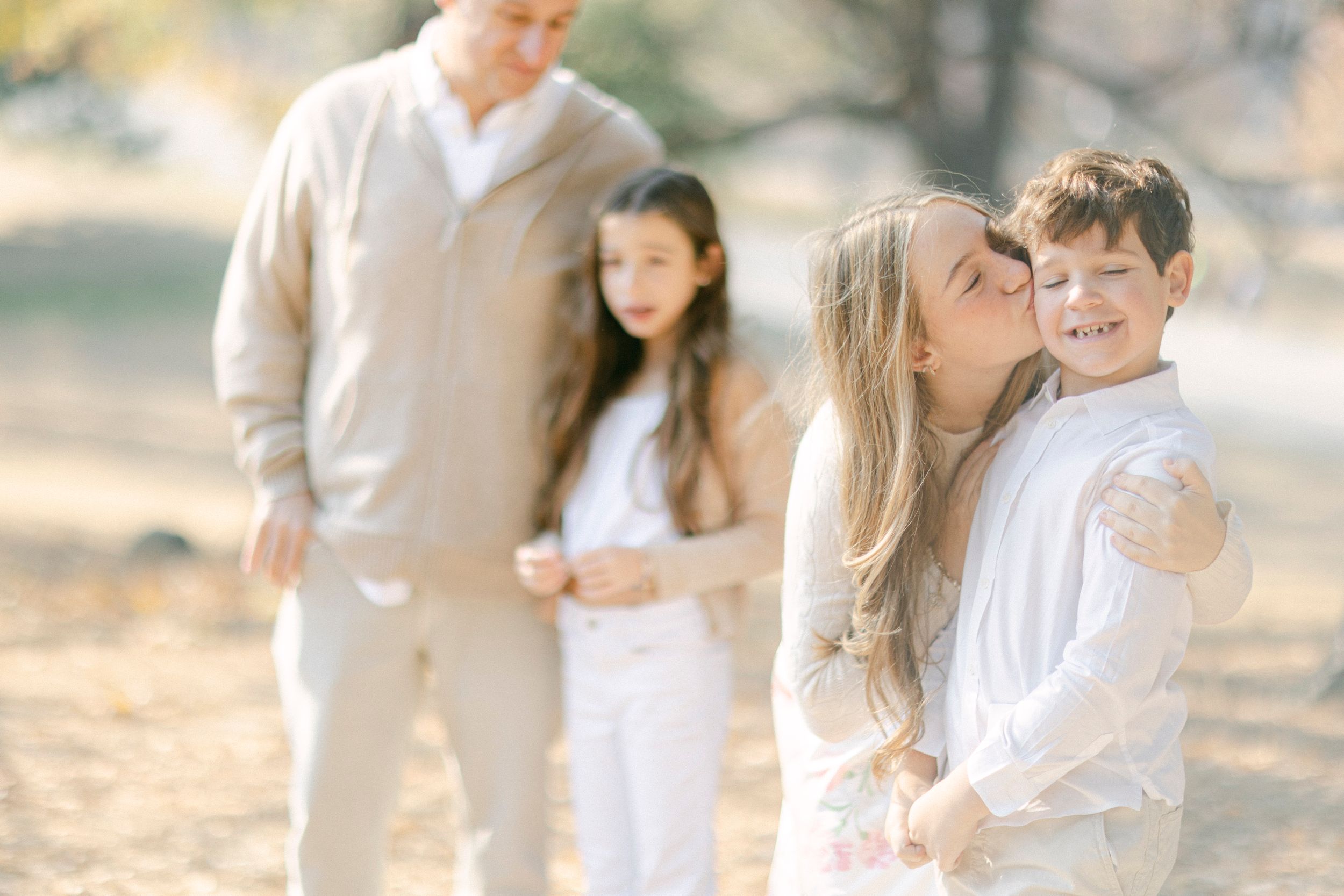 Family of four poses together outdoors wearing coordinated light colored outfits.