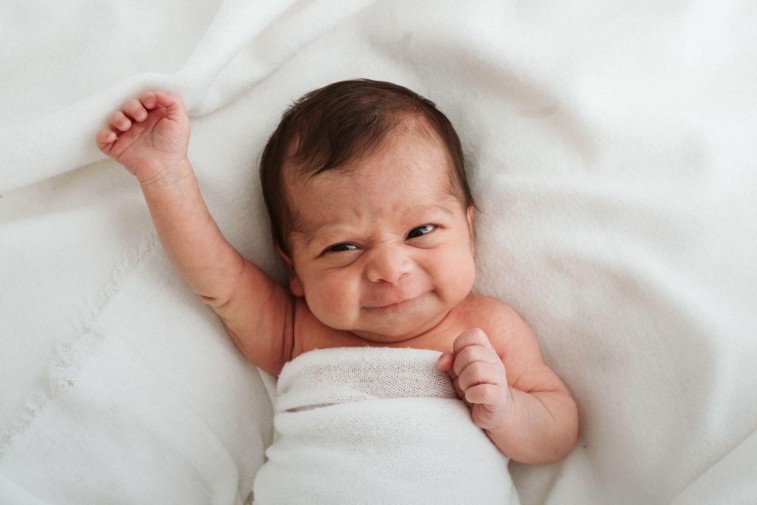 Newborn baby sleeping peacefully on white bedding in natural light.