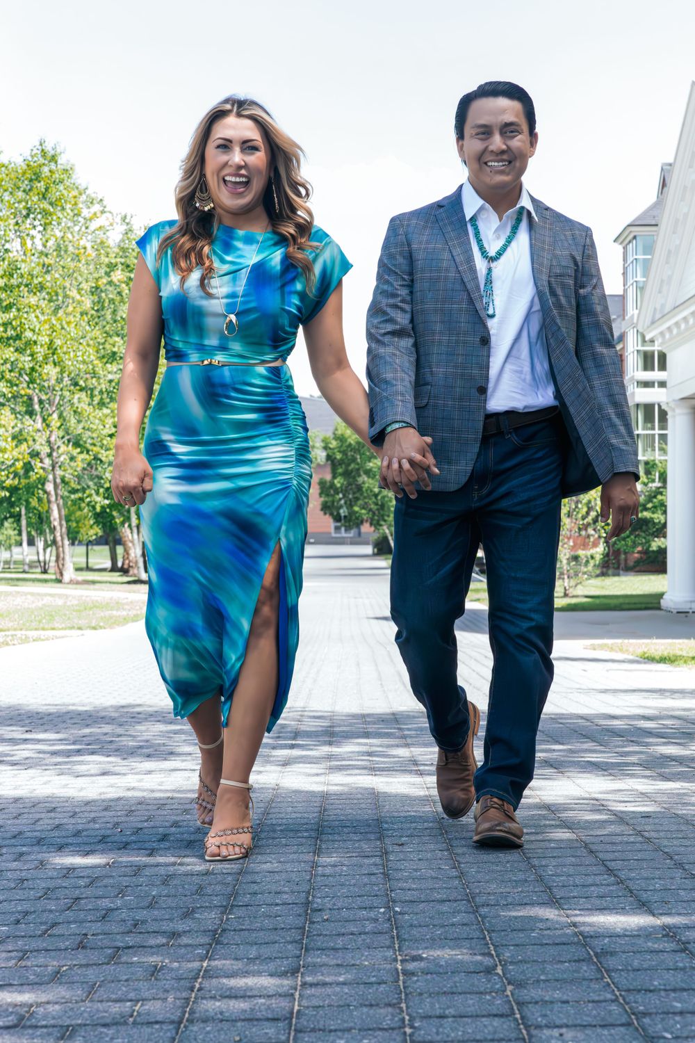 Couple walking and laughing together on a paved path, with the person in blue dress holding papers.