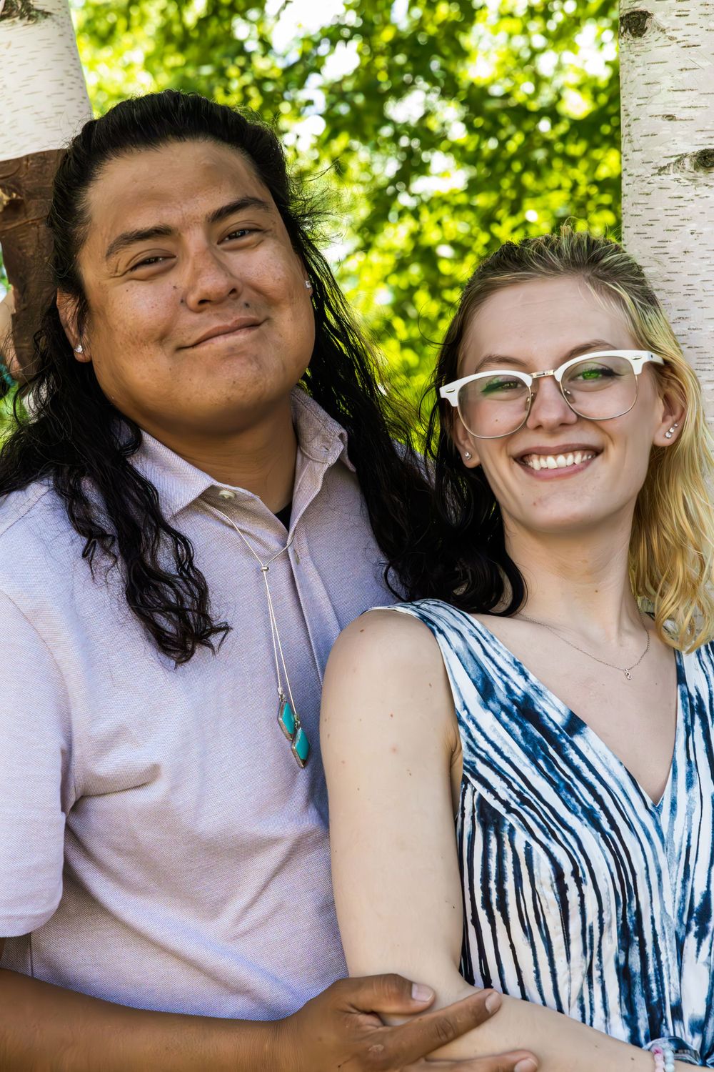 Two people share a tender moment while sitting together against a birch tree backdrop.
